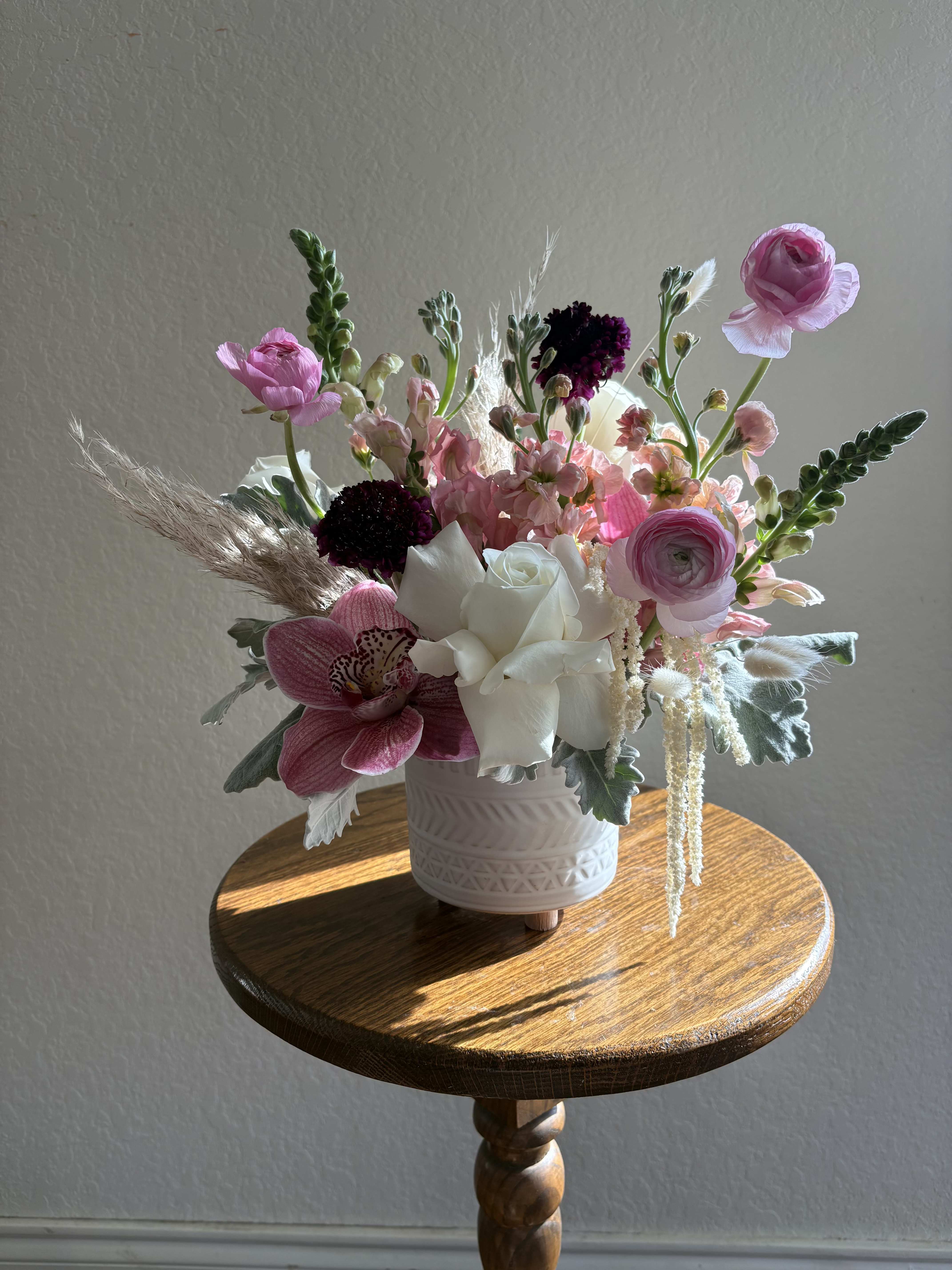 Foxy Bloom - A flirtatious blend of soft pinks and whites with boho textures that feel straight out of the 70s. Designed in a warm terracotta vase, this arrangement layers fluffy pampas grass, playful bunny tails, and silvery dusty miller with dreamy blush and white blooms. Earthy yet feminine, Foxy Bloom is the perfect retro-chic statement for your home, office, or as a gift for someone who radiates flower child energy.