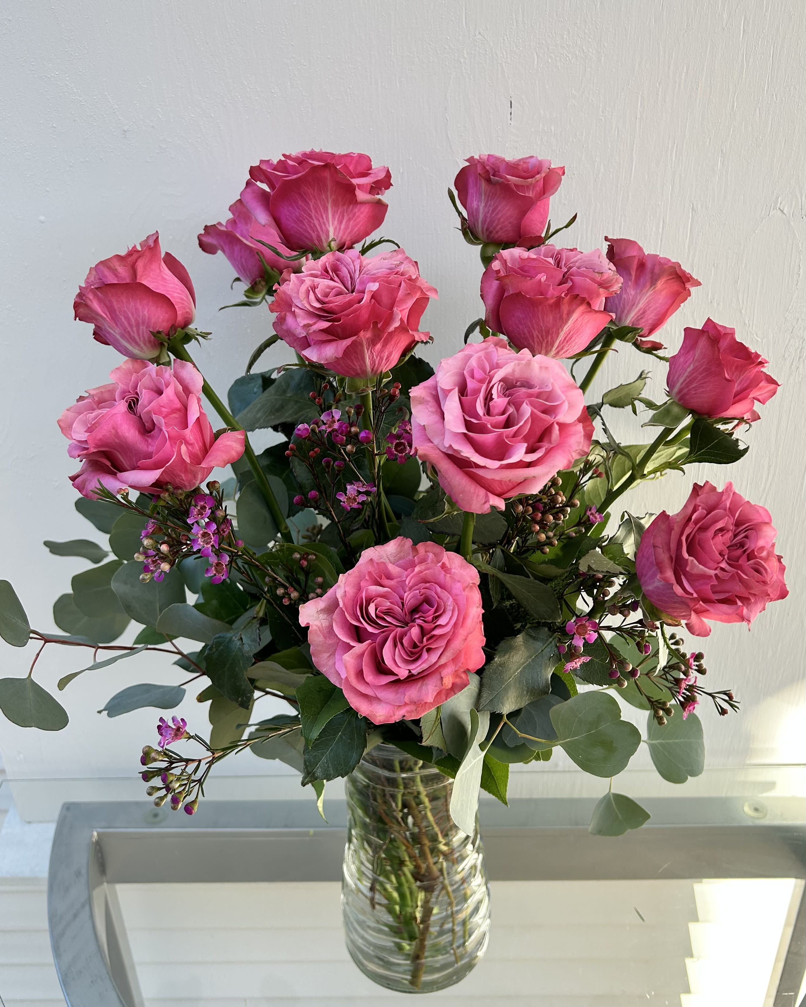 Country Blues - 12 country blues roses pinkish lavender roses in a vase with greens and wax flower filler. 