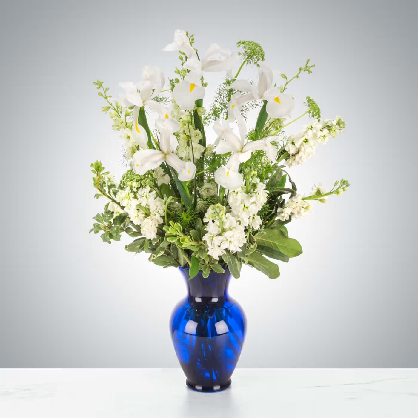 Crystal Symphony by BloomNation™ - This arrangement includes white iris, white stock, white snapdragons, and queen anne's lace in a blue vase. Send your condolences with Crystal Symphony by BloomNation™™.  Approximate Dimensions: 22"D x 30"H