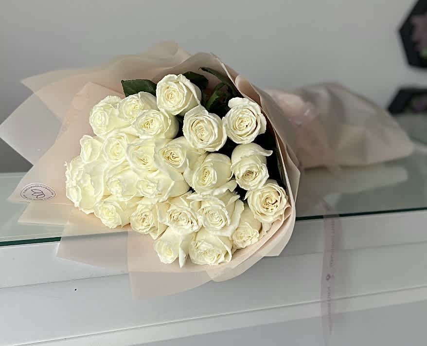 25 White Roses Bouquet - Classic and graceful, our 25 White Roses Bouquet is a timeless symbol of purity, elegance, and sincerity. Handcrafted with premium white roses, wrapped in soft pastel paper, and tied with a satin ribbon, this bouquet radiates sophistication. Whether celebrating love, offering condolences, or sending a thoughtful gesture, it speaks volumes without a word.   •    25 fresh white roses carefully selected for beauty and quality     •    Wrapped in elegant pastel paper with satin ribbon     •    Represents purity, grace, respect, and everlasting love     •    Perfect for weddings, anniversaries, sympathy, or elegant gifting  VASE NOT INCLUDED
