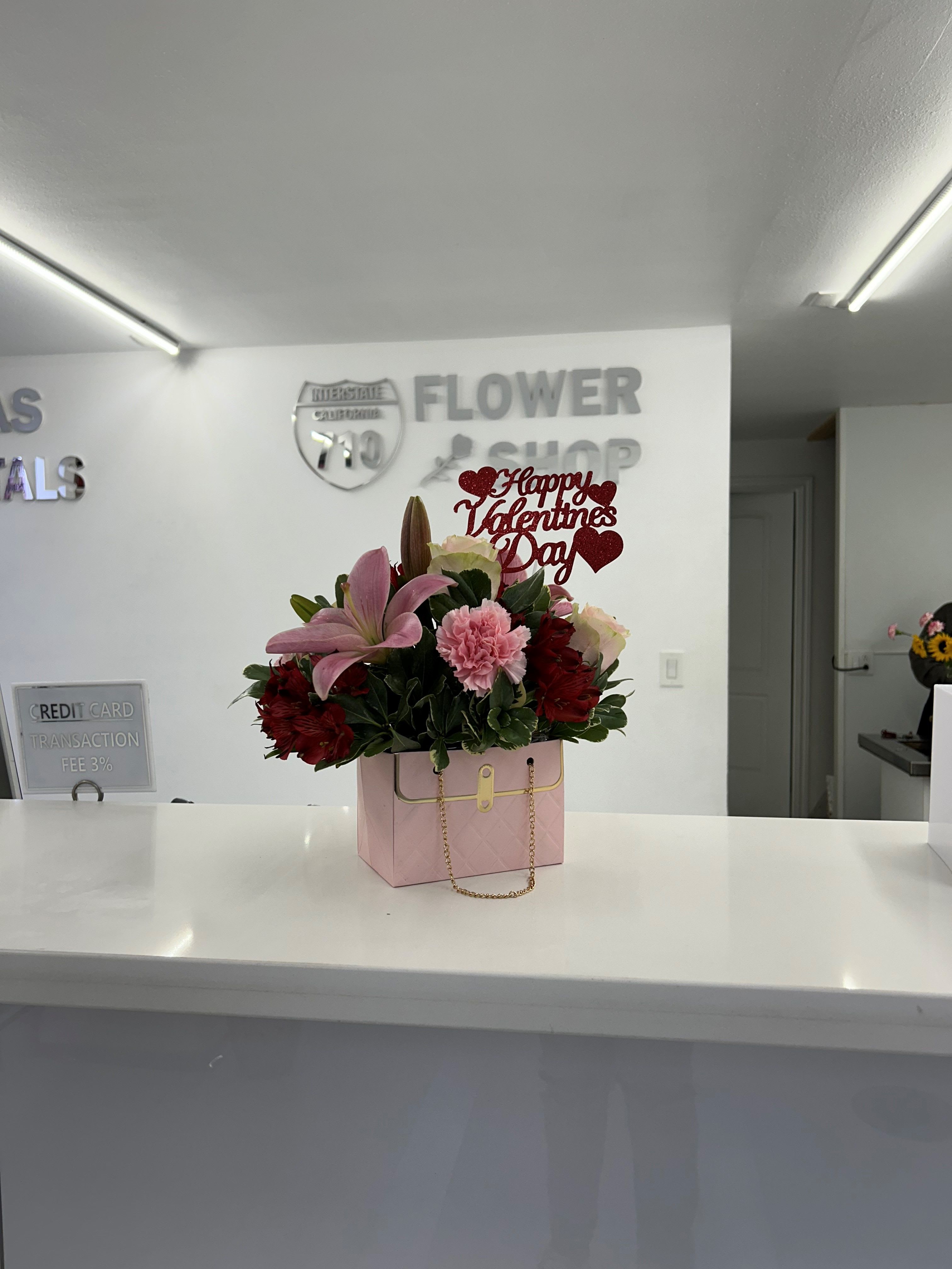 Pink Purse Arrangement - A cute pink purse arrangement with beautiful flowers! Comes included with valentines day sign! Heart Box comes in Pink, Black, and White with a mixture of flowers. If you'd like a specific color please leave note in instructions! (Chose your choice of color. If we do not have the same sign, chosen box color available or the same flower as photo we will add substitute for next available)