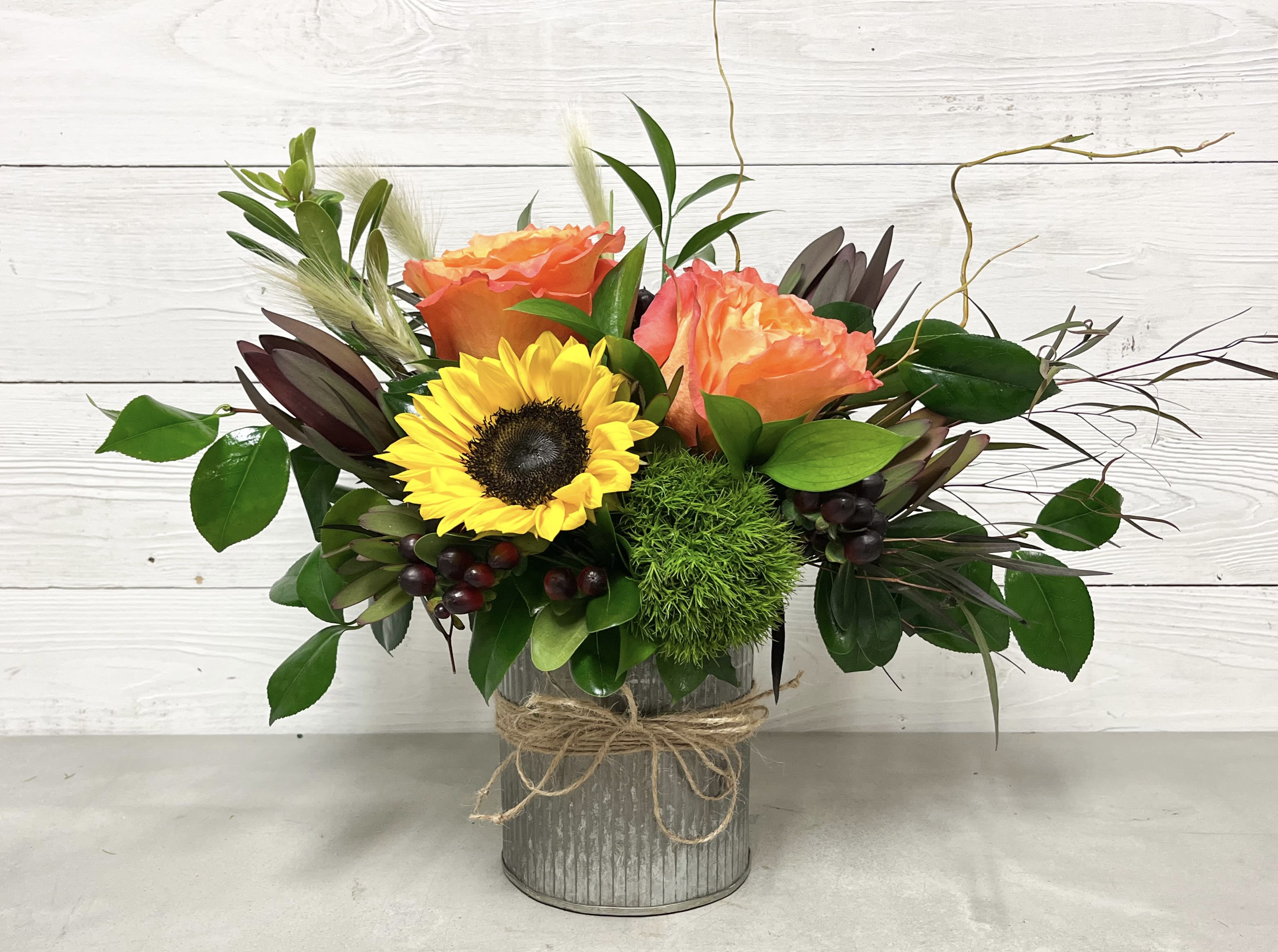 Dolly - This little country arrangement features a fall mix of sunflowers, free spirit roses, dianthus, and hypericum, accented with greens and filler in a keepsake corrugated tin container. 