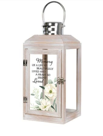 Carson In Memory of Lantern - Carson lantern built with white composite wood and a stainless-steel silver finish top.  Features a built-in battery powered flicker candle.  Lovely scene on front panel is inscribed with sentimental quote.  "In memory of a life so beautifully lived and a heart so deeply loved."  14 x 5 3/8 x 5 1/2.  A small silk flower/bow will be added to the top of the lantern.  
