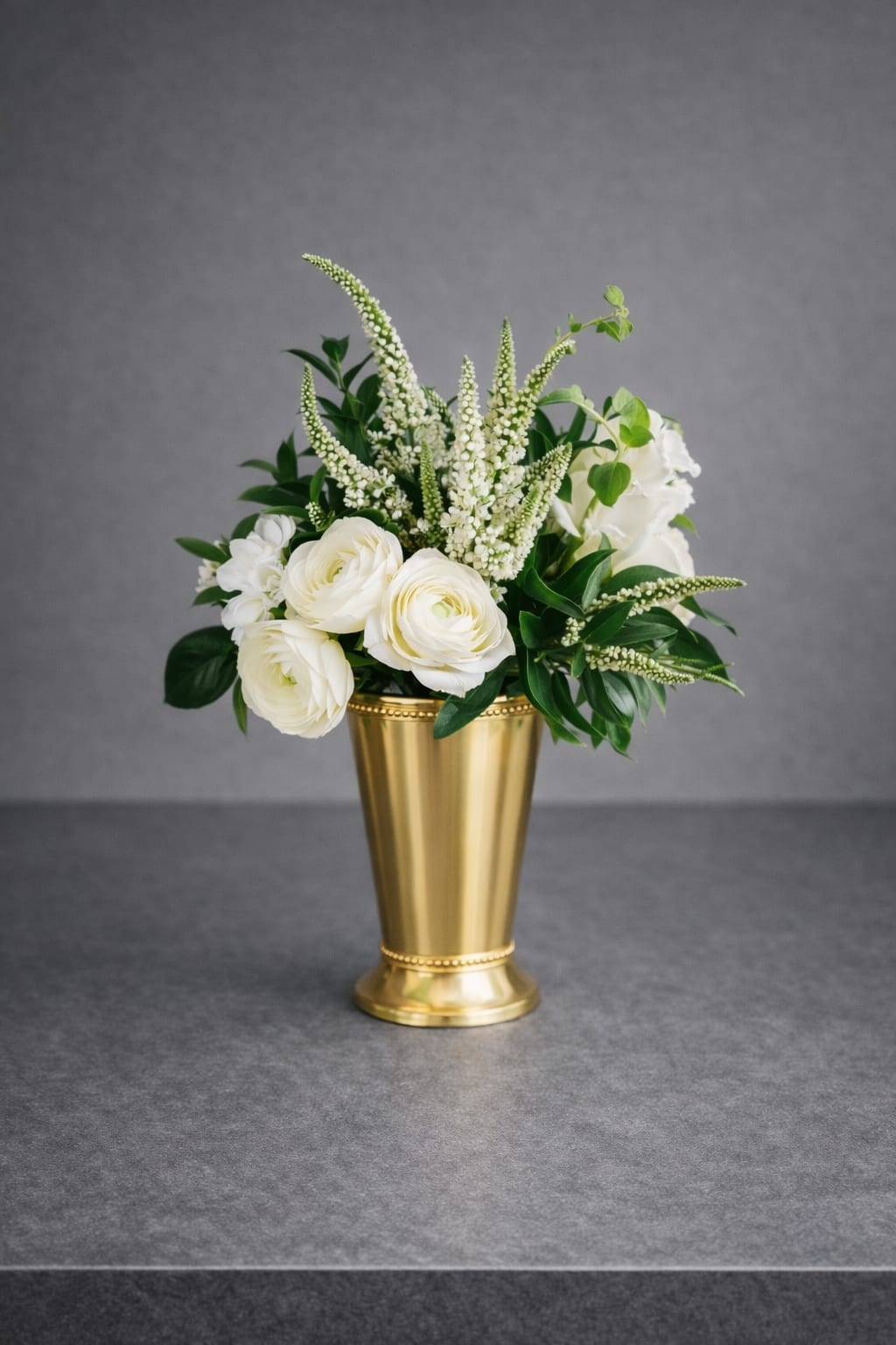 White Garden Muse - A modern garden-style arrangement featuring delicate white ranunculus, airy veronica, and fresh greenery. Designed with a clean, minimalist feel, this elegant petite floral piece brings refined beauty to any space.  Approximately 10-12 inches tall, 7-8 inches wide. 
