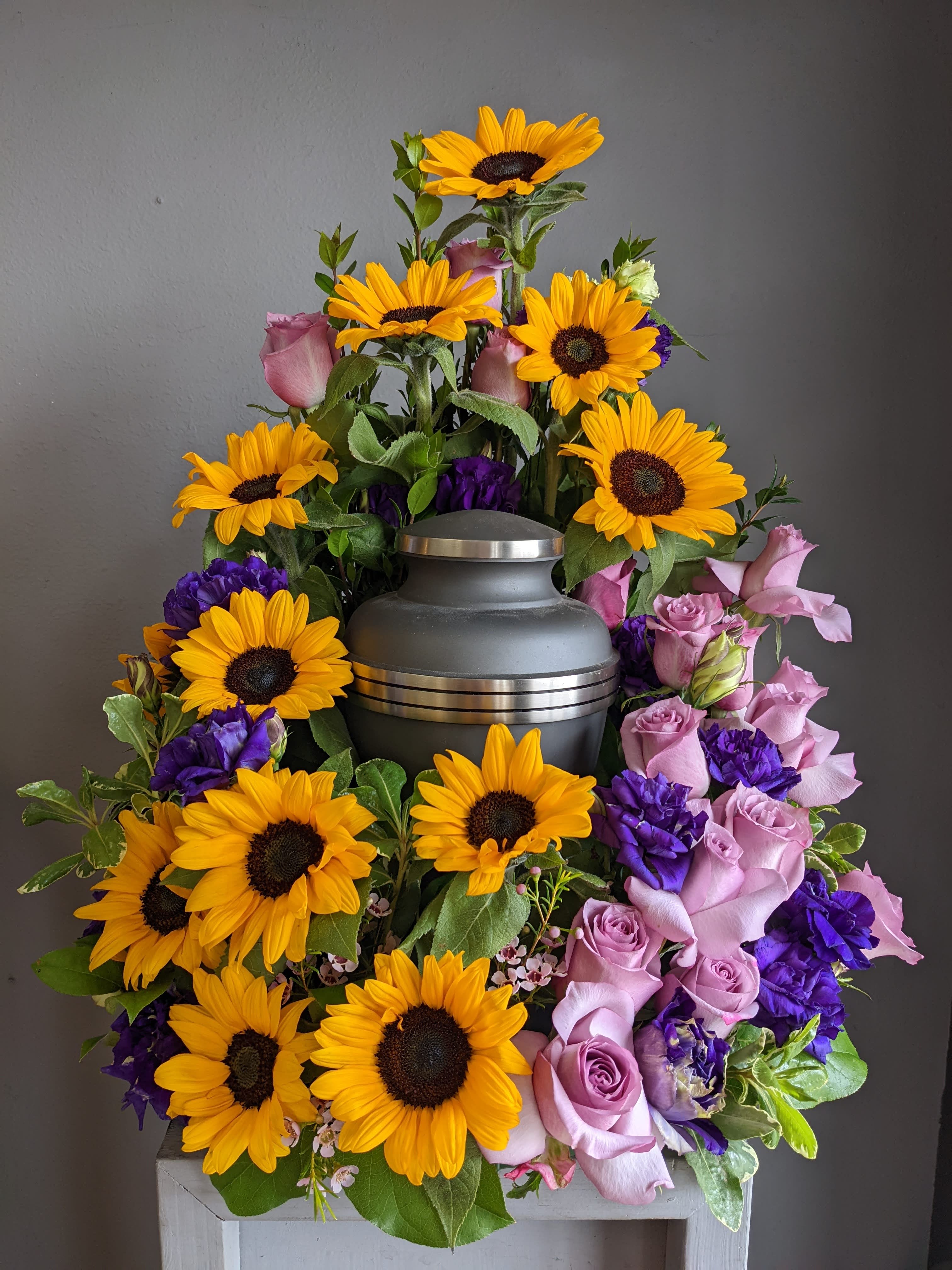 FUNERAL URN WREATH - For the Love of Sunflowers 116 - This is a stunning option for a memorial service with soft colors. This open ring wreath will be designed with a 10.5” ring form with the urn resting in the middle. This piece features the beauty of purple and yellow with sunflowers, roses and lisianthus in a beautiful piece for a cremation or memorial service.   **This is a piece for a funeral or memorial service. Please place the order at least 2 days prior to the service to guarantee a certain arrangement. Anything sooner and we cannot guarantee it will match the picture. These pieces can be customized to the color of your choice. The flowers may vary depending on availability of the flowers, special requests and quality of the flowers we have in stock. If you have a special request please add it to our special instructions when placing your order. If you have any questions please don’t hesitate to call. 714 289 1123**
