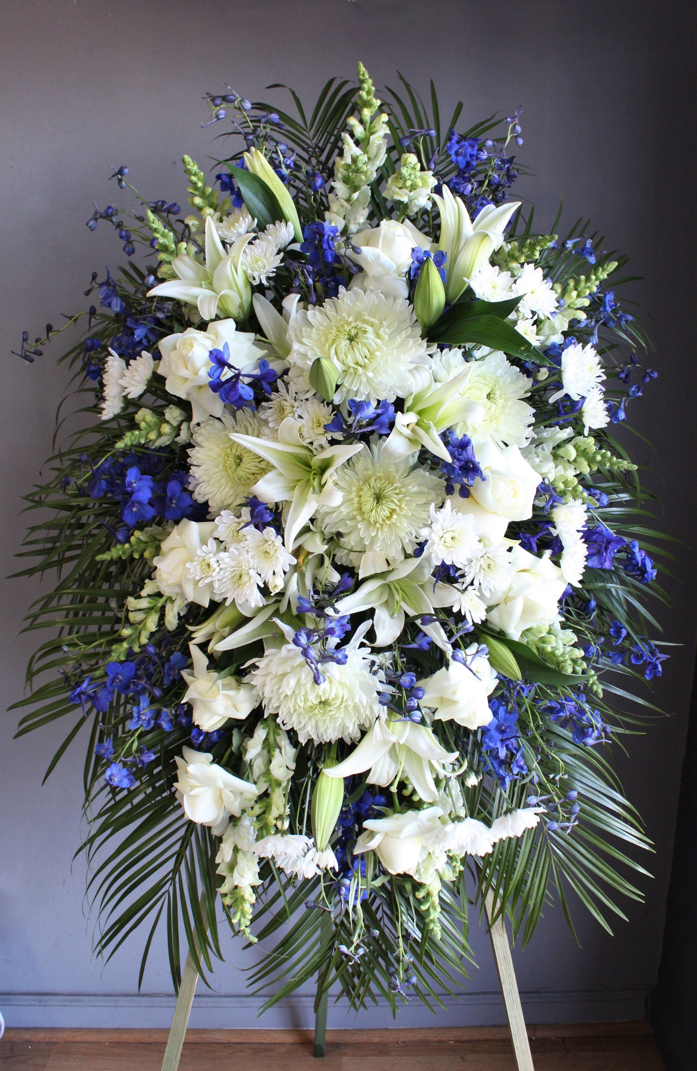 FUNERAL STANDING SPRAY - Spectacular Send Off 50 - This is a wonderful option for a funeral service, church or graveside . This standing spray is a one sided flower arrangement on a 5' easel (easel included). This piece is an impressive mix of whites and blues with flowers like mums, roses, lilies and delphinium. This will make a beautiful display for any service or memorial with just the right amount of color.  The first image above shows the standard "Spectacular Send Off" standing spray. The second image is an example variation of the same spray at the same price. If your are looking for a variation from the standard blue and white, please note that in your order or give us a call.   **This is a piece for a funeral or memorial service. Please place the order at least 2 days prior to the service to guarantee a certain arrangement. Anything sooner and we cannot guarantee it will match the picture. These pieces can be customized to the color of your choice. The flowers may vary depending on availability of the flowers, special requests and quality of the flowers we have in stock. If you have a special request please add it to our special instructions when placing your order. If you have any questions please don’t hesitate to call. 714 289 1123**