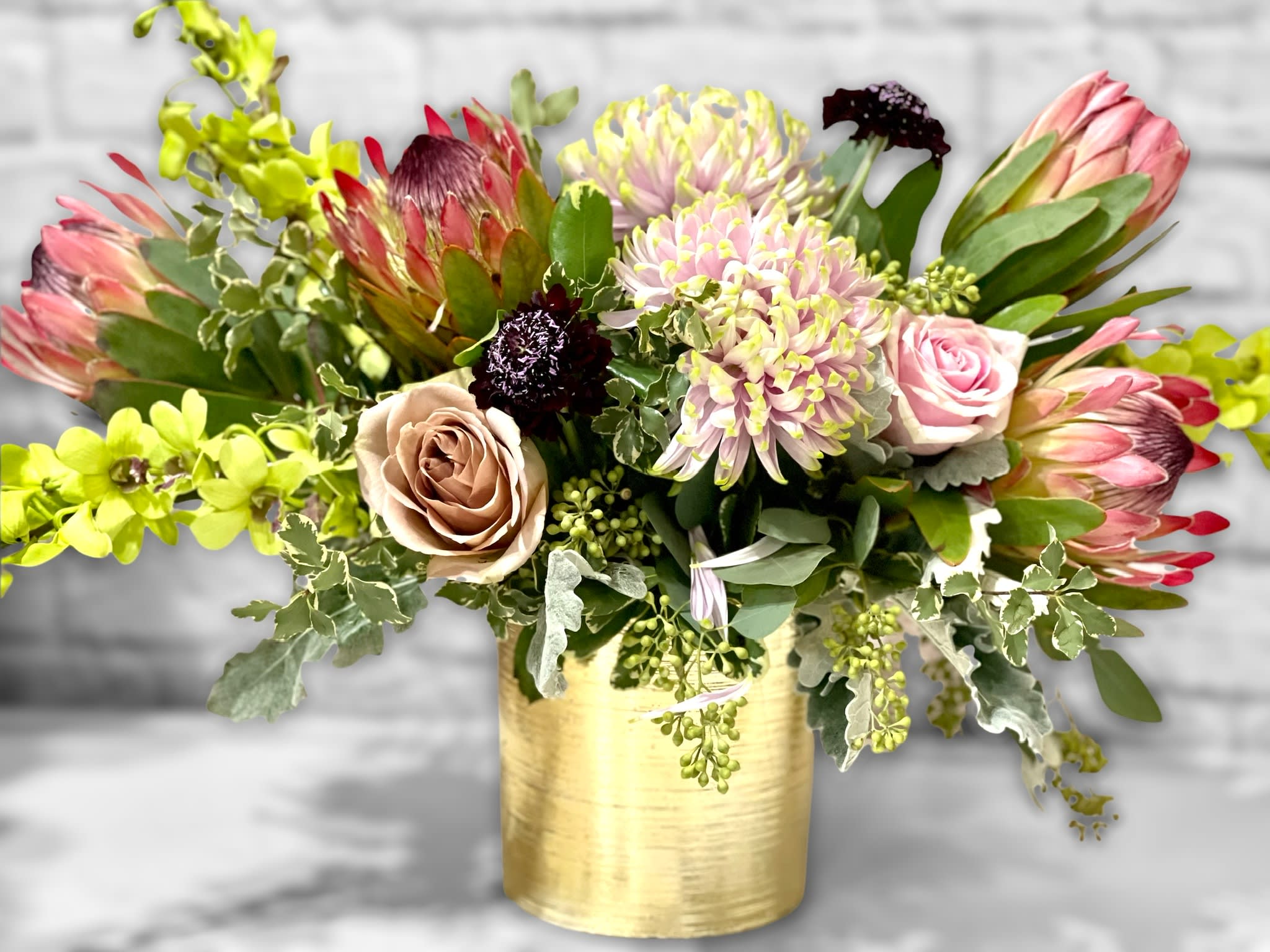 Warm Winter Beauty  - A stunning bouquet of blooms for any occasion! Several Pink Mink protea serve as a bold focal point and are surrounded by roses, orchids and large specialty chrysanthemums. Artfully arranged in a gold vase. A real show stopper! 