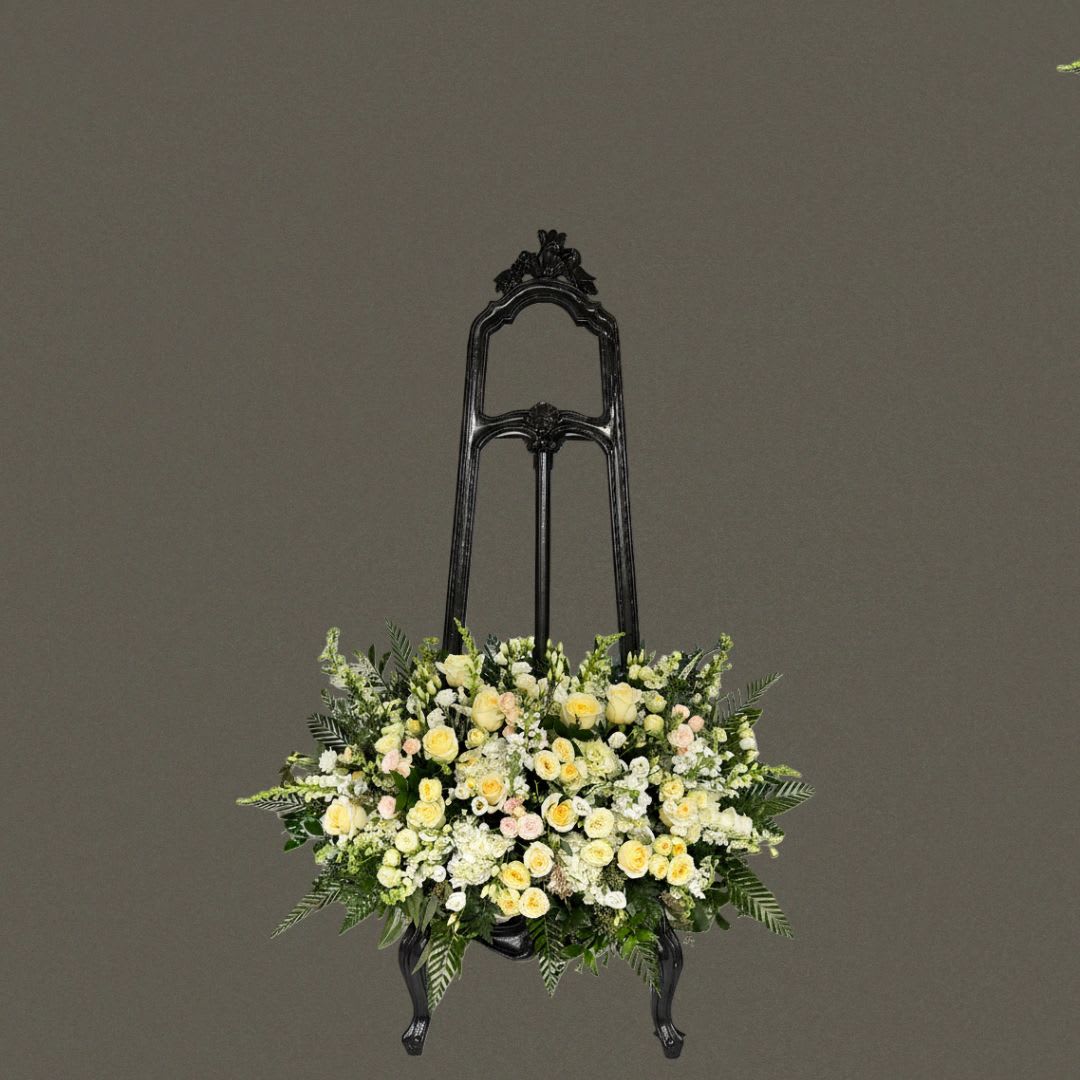 Gentle Tribute Standing Spray - A soft and elegant standing spray designed to convey sympathy, comfort, and quiet remembrance. This arrangement features a refined blend of ivory and cream roses, spray roses, delicate filler flowers, and layered seasonal blooms, surrounded by rich, textured greenery. Designed for display on an easel, its full, rounded shape creates a graceful focal tribute suitable for funeral and memorial services. The gentle color palette offers a warm, peaceful expression of honor and heartfelt condolences. Easel not included.