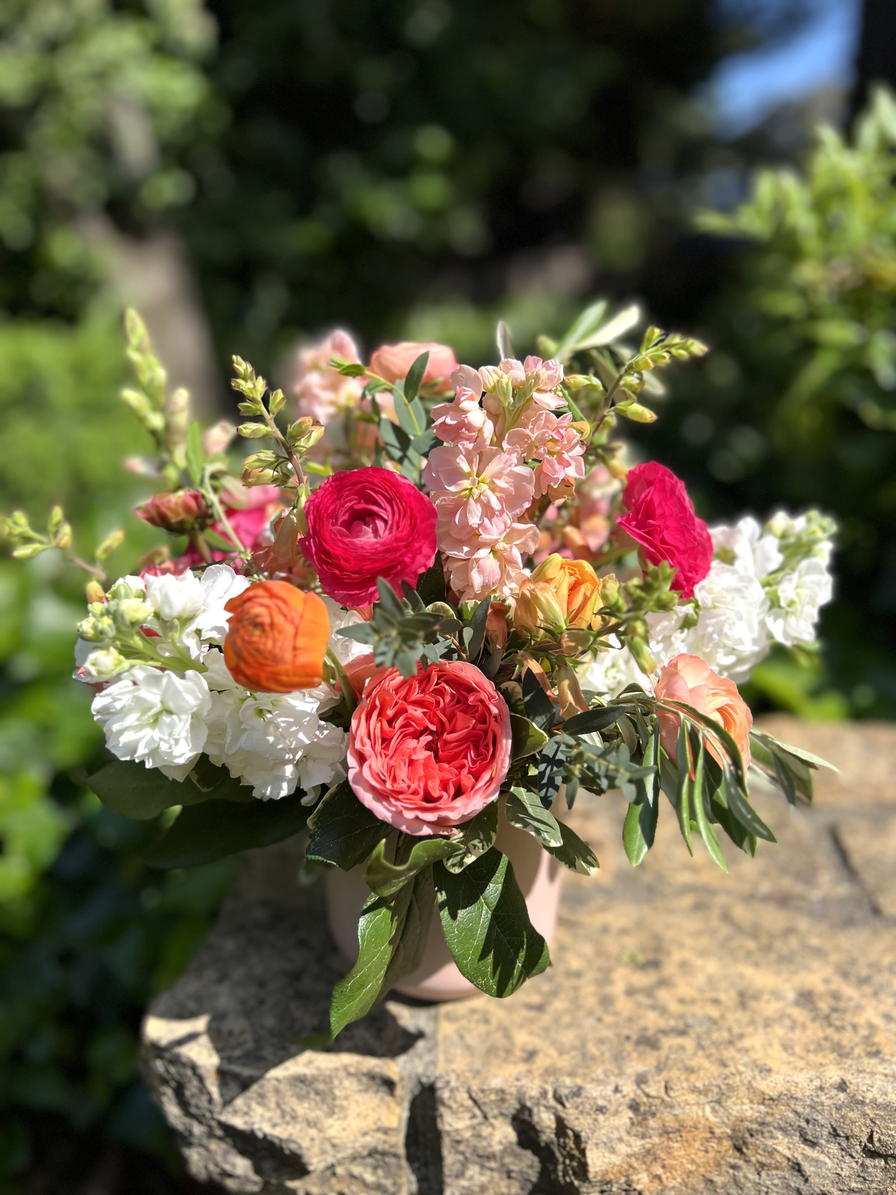 Summer Sorbet  - Corals, peaches, hot pink, and orange make up this beauty; featuring stock, garden roses, tulips, ranunculus and foxglove in a soft blush ceramic container. 