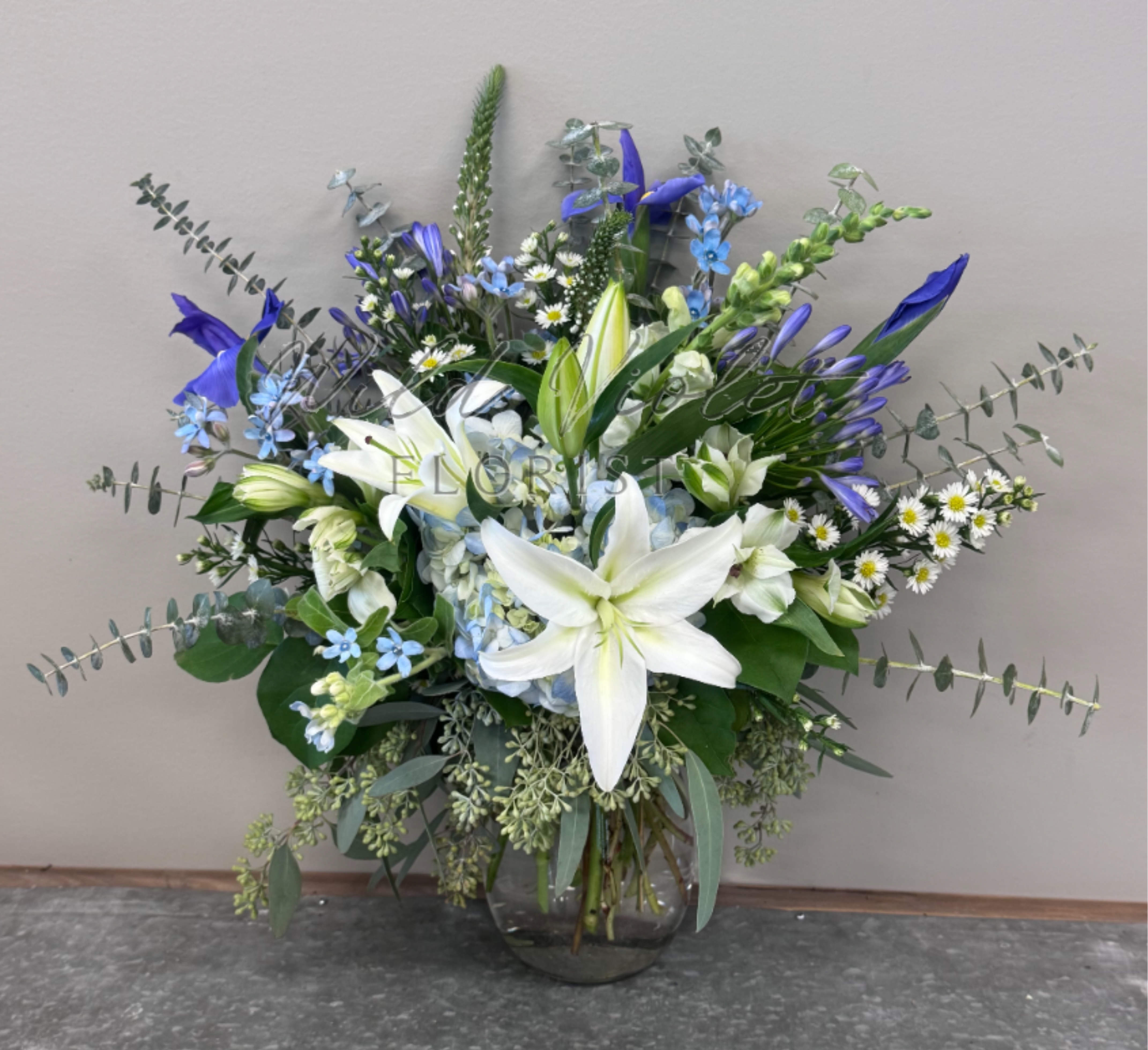 December Tanzanite Bouquet - Birthstone Collection What better way to celebrate your loved one's birthday than with our December Tanzanite Bouquet! Hand-designed with a cool gathering of pale and dark blue blooms, whites and silver eucalyptus, it’s a thoughtful sentiment filled with the icy, stunning beauty of a tanzanite stone.  ATTENTION! If you are ordering this arrangement on a different month other than what it's respected month is, there will be substitutions for certain flowers depending on seasonal availability. We will stay within the same color scheme and design style!  PLEASE NOTE: Florist reserves the right to make modifications to the design based on seasonality and accessibility of blooms and vases. Any modifications made will honor the palette, intent, and feeling of the pictured design. Contact floral designer directly with any specifications or concerns.