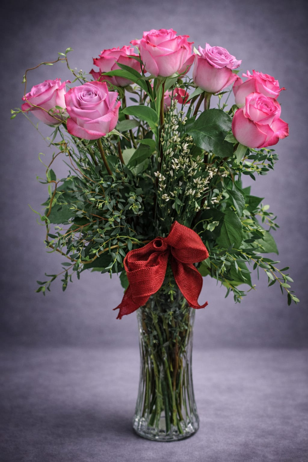 One Dozen Purple Roses - A classic dozen roses in a purple tone with filler and greenery accented with a ribbon.