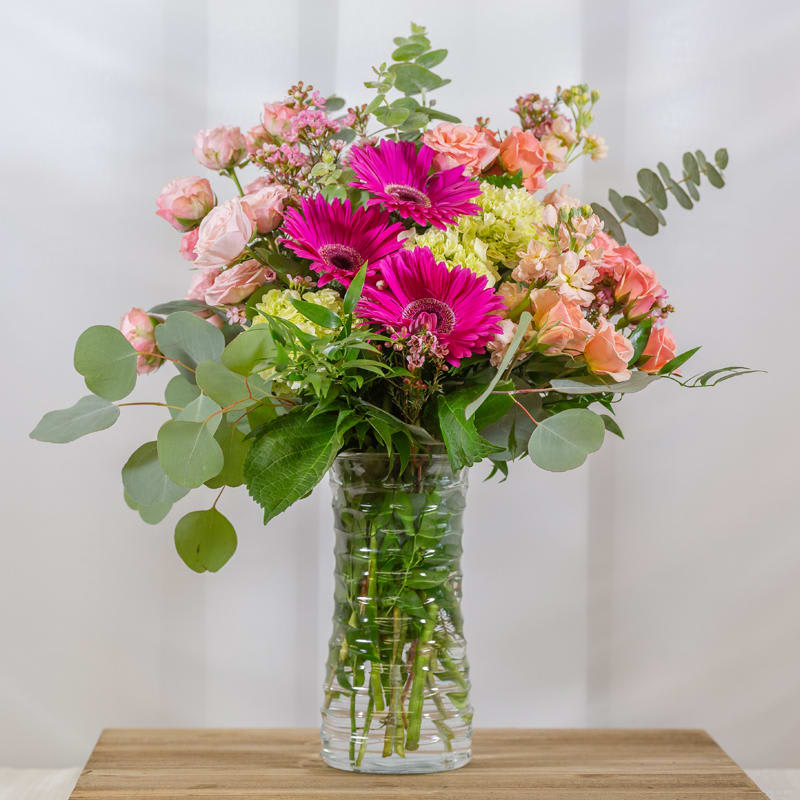 Timeless Beauty - This tall glass vase features Mini green hydrangea, hot pink gerbera daisies, prink spray roses, wax flower and eucalyptus. 