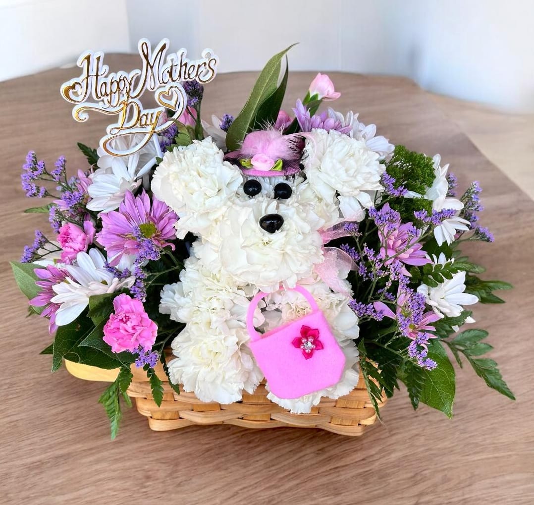 Mama Paws (New for 2026) - Unleash Mom's smile with our truly original, colorful dog-shaped floral creation. The mother of all our signature A-DOG-Able arrangements, this bright gathering of white carnations, assorted spring colorful flowers, hand-crafted in a wicker basket with an assorted colored feathered hat with a Felt HANDBAG  Hand-designed a-DOG-able arrangement of white carnations,  Crafted in the shape of an adorable dog, complete with eyes, nose, and a stylish assorted color feathered hat. Designed in a wicker basket Arrangement measures approximately 11"H x 11"L We only use the freshest flowers available so floral colors and varieties may vary due to availability.