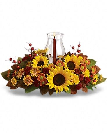 Sunflower Centerpiece - Symbolizing warmth and happiness, it is no wonder the sunflower is a quintessential ingredient in so many fall bouquets. This centerpiece maximizes the joy of sunflowers by arranging them with a bevy of fall flowers, foliage and a cranberry hued candle under hurricane glass. Along with brilliant sunflowers, you'll find yellow spray roses, bronze and rust chrysanthemums, red berries, magnolia leaves and of course an elegant tapered candle inside a hurricane vase. 