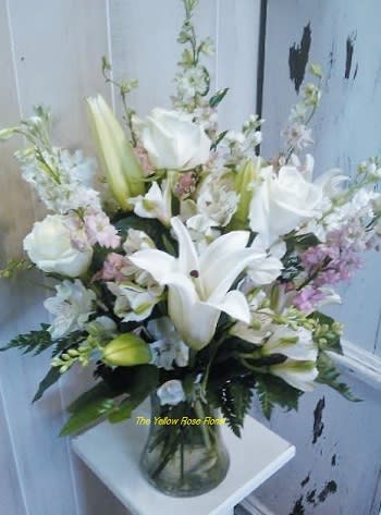 White Lily Enchantment - This lovely arrangement consist of white lilies, white roses, alstroemeria greenery and a touch of ever so light pink larksburg gathered in a clear glass vase. 