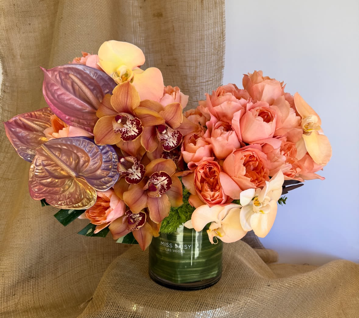 C'est La Vie - That's life and this is the perfect arrangement! Garden style overflowing with tinted anthirium, phaeonopsis, garden roses, cymbidiums, and other beautifully toned elements.