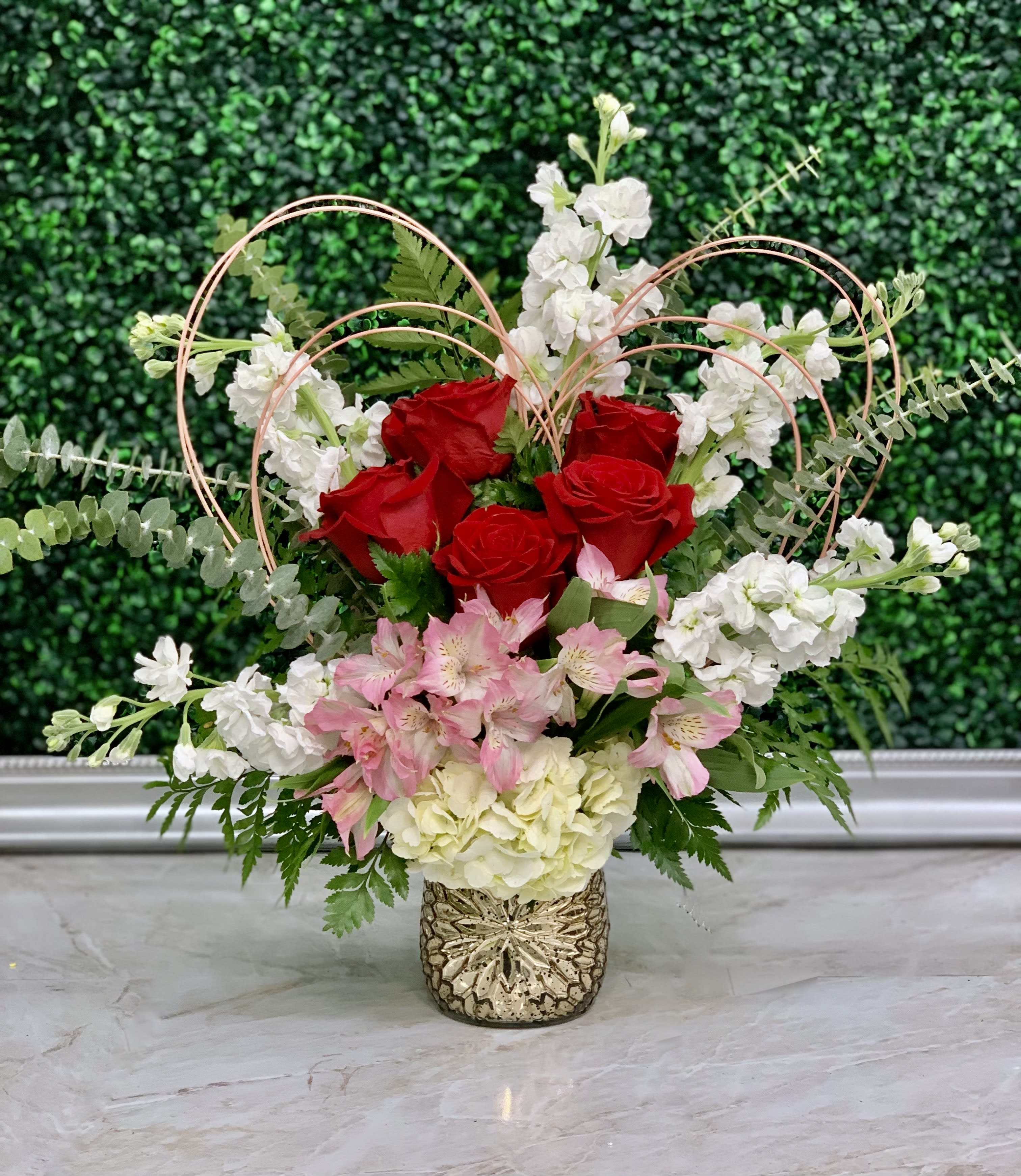 Tiffany Heartish - This adorable arrangement is nestled in a textured rose gold vase filled with stock, red roses, hydrangeas, alstromeria and eucalyptus. Topping off this cutie is a medallion hand crafted heart!