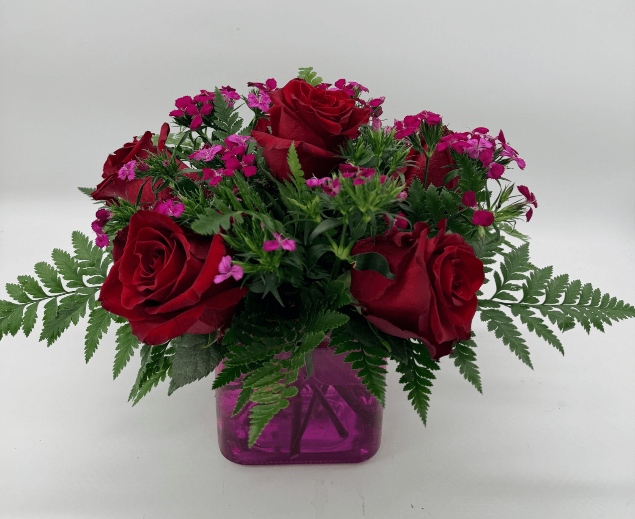 Roseberry Bliss - A charming mix of rich red roses, vibrant  accent flowers, and lush greenery arranged in a contemporary glass cube, this piece brings a sweet pop of color to any space.  Filler and vase may vary depending on availability.