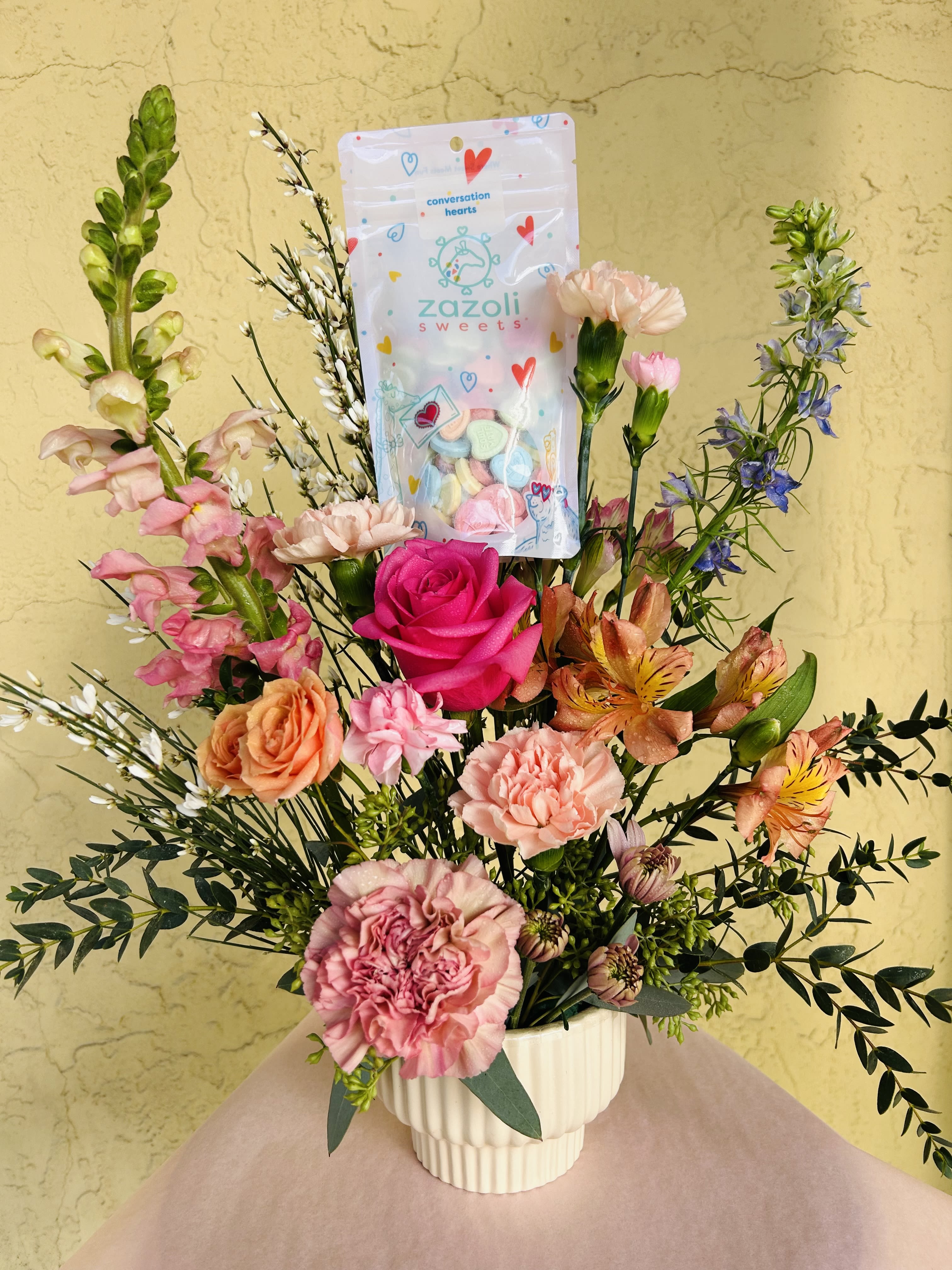 Candy Hearts Bouquet  - This sweet design is perfect for showing someone you care! Designed in a beautiful, petal pink ceramic pedestal vase that can be reused and filled with fresh candy colored blooms. Includes conversation hearts for someone deserves a treat! 