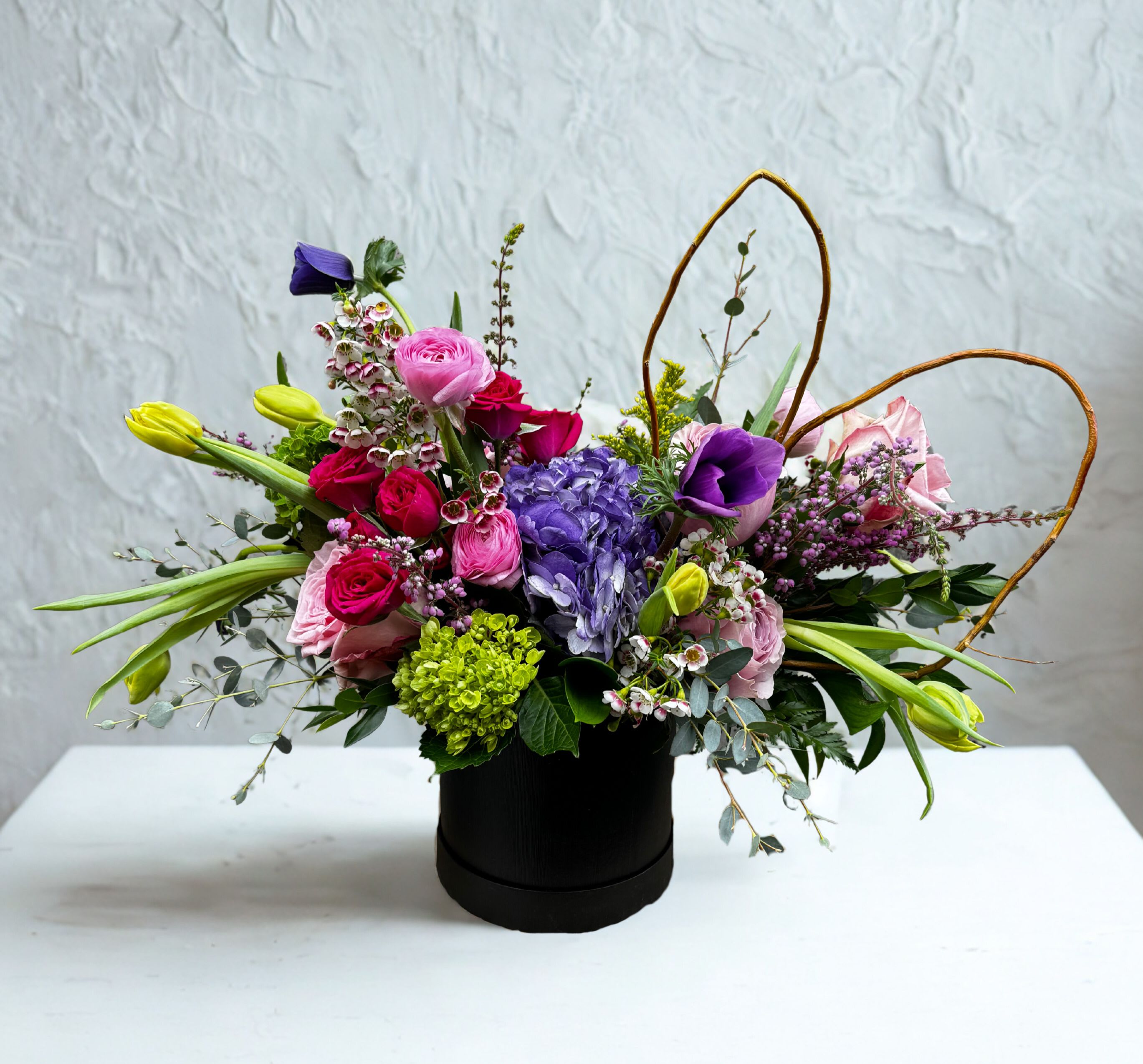 Hillsides Petals &amp; Poetry - A lush and romantic arrangement of soft pink ranunculus, classic roses, and delicate seasonal blooms, artfully accented with flowing greenery and graceful branches. Designed to capture the feeling of being in love.