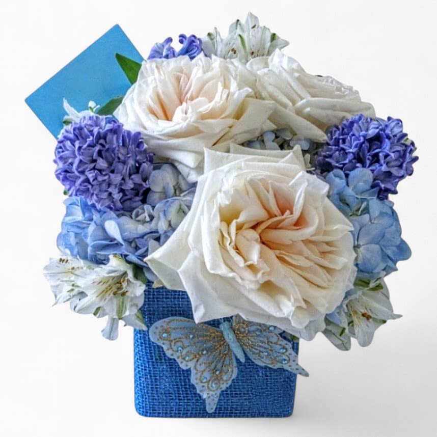 Blueberry And Creme Bouquet Designer's Choice - Send this beautiful bouquet today for every occasion to make them smile with it's lovely mixed blue and vanilla blossoms of the day roses orchids hydrangeas and more arranged in a modern glass cube vase. Always  made extra special and unique each time. Send happiness.