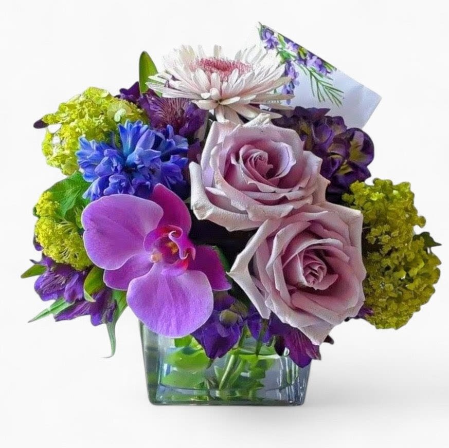 Lavender Mint Beauty Designer's Choice - Send this pretty bouquet today to make them smile with it's lovely mixed lavender and green blossoms of the day roses orchids and more arranged in a modern glass cube vase. Perfect to send for every reason. Always made extra special and unique each time. Send them happiness.