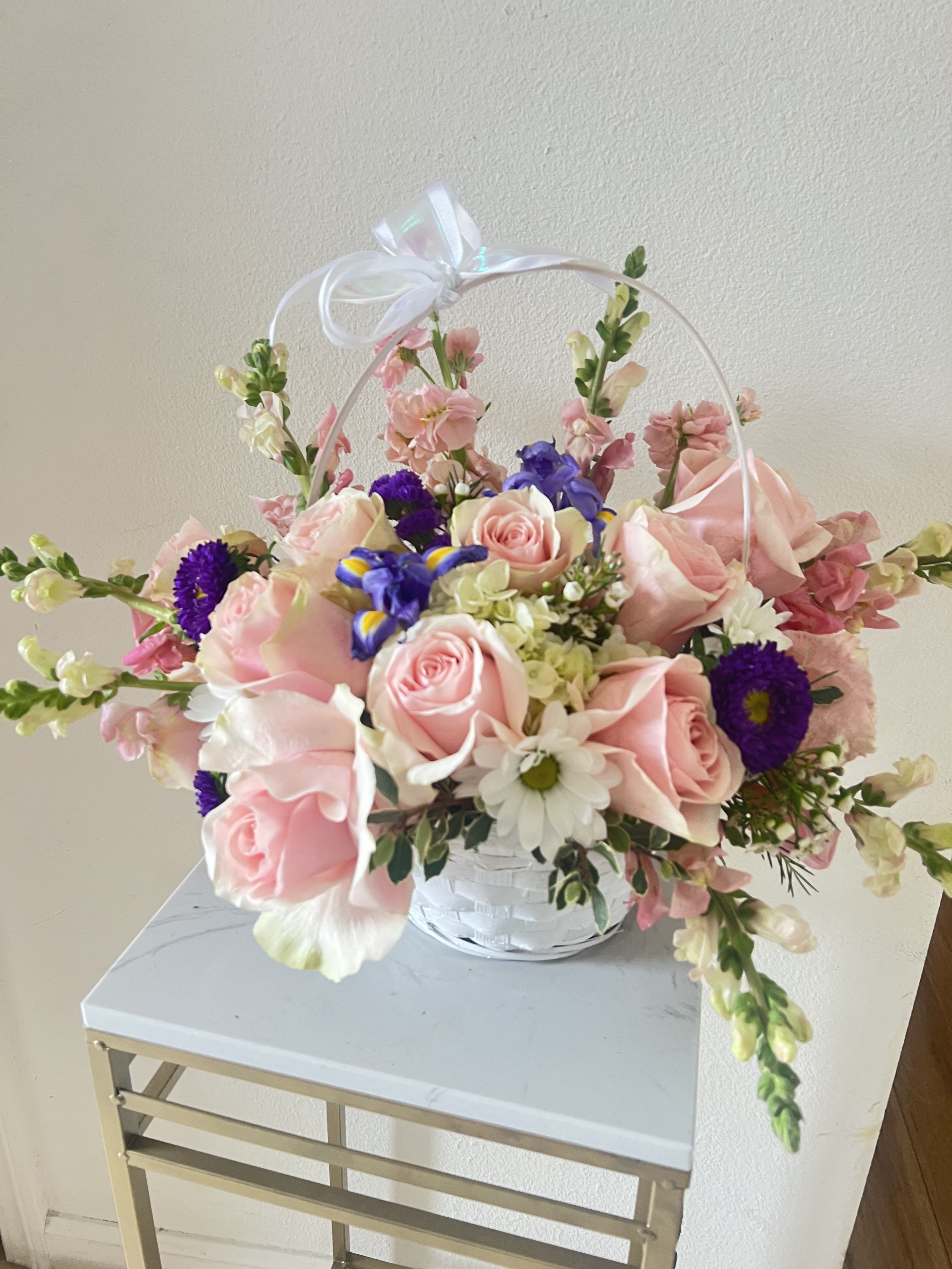 A Touch of Sweet Basket - A Touch of Sweet Basket, is the perfect choice for sympathy, birthdays, or simply because gifts. Featuring premium pink roses, lavender snapdragons, fresh white chrysanthemums, purple statice, and lush green hydrangeas, this bouquet is hand-arranged in a white wicker basket and finished with a pastel satin bow. A timeless gift to brighten someone’s day.