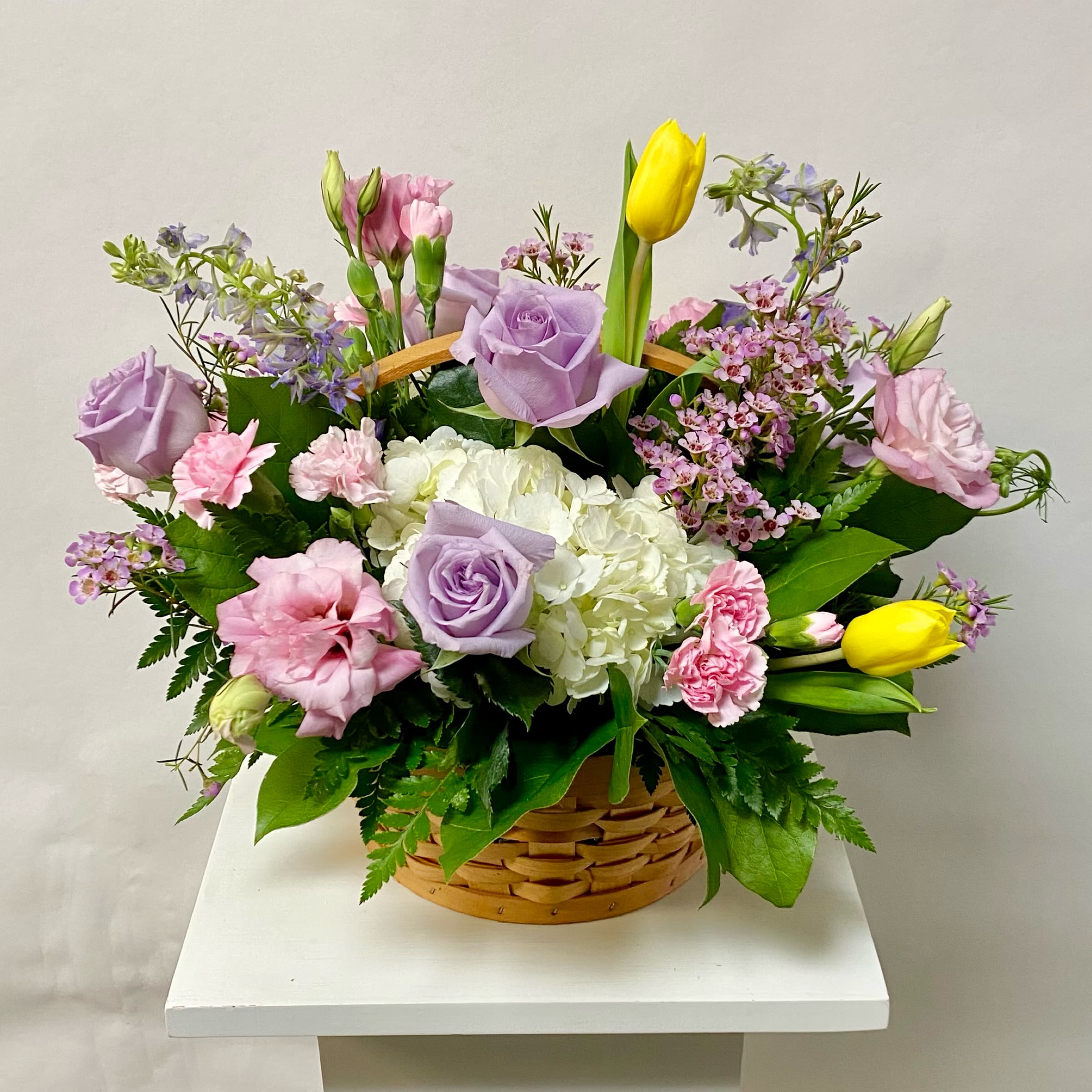 Sending Hugs Basket - This Basket Arrangement includes White Hydrangea, Light Pink or Lavender Lisianthus, Lavender or Light Pink Roses, Wax Flower Filler, Tulips and Larkspur. Or as Similar as Possible. 