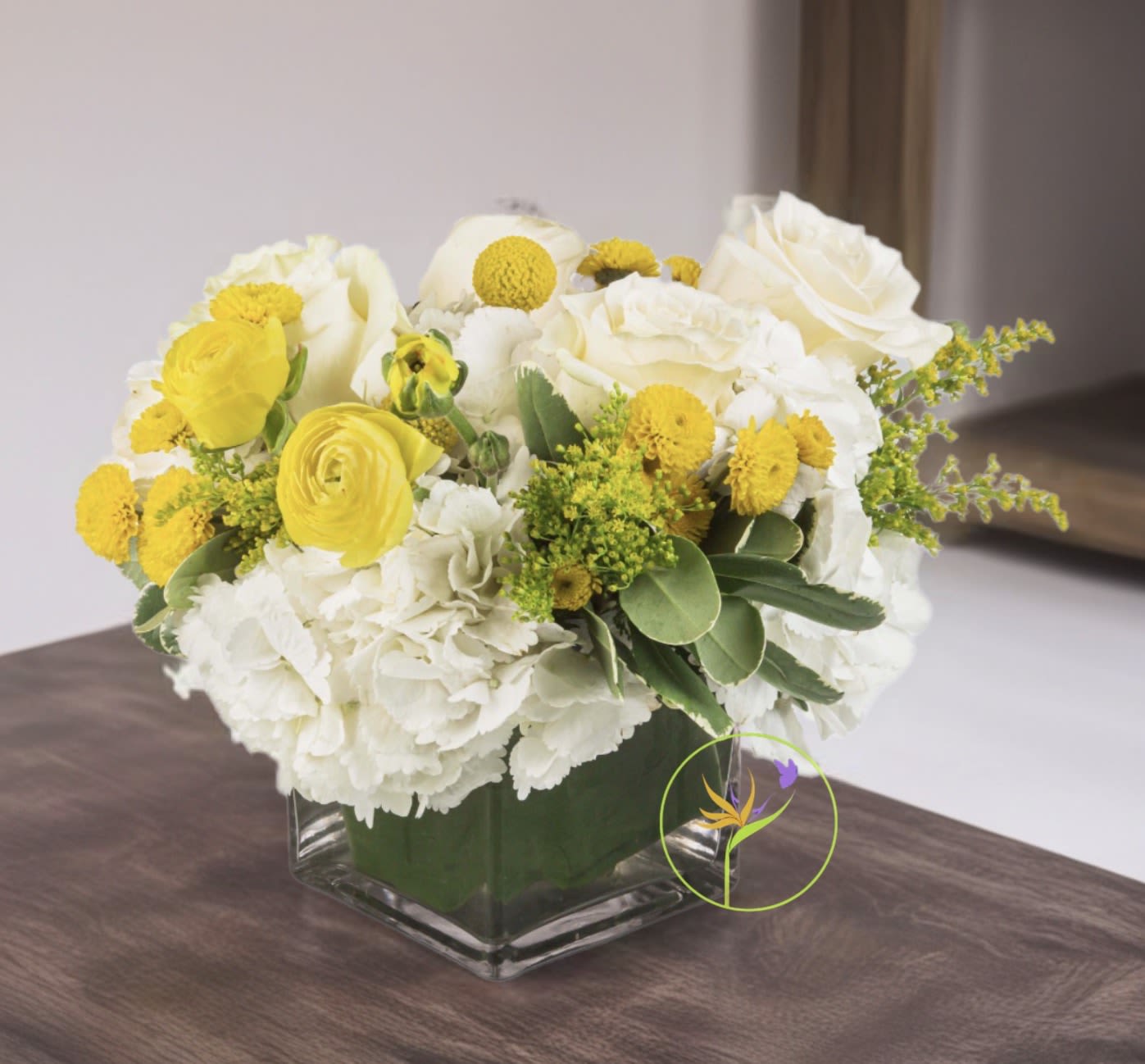Honeybee by BloomNation™ - This white and yellow arrangement includes cream roses, button mums, and ranunculuses. Honeybee by BloomNation™ is the perfect way to brighten a day! Send a little joy and make somebody feel good. Perfect to send as a get well soon present or just because! 