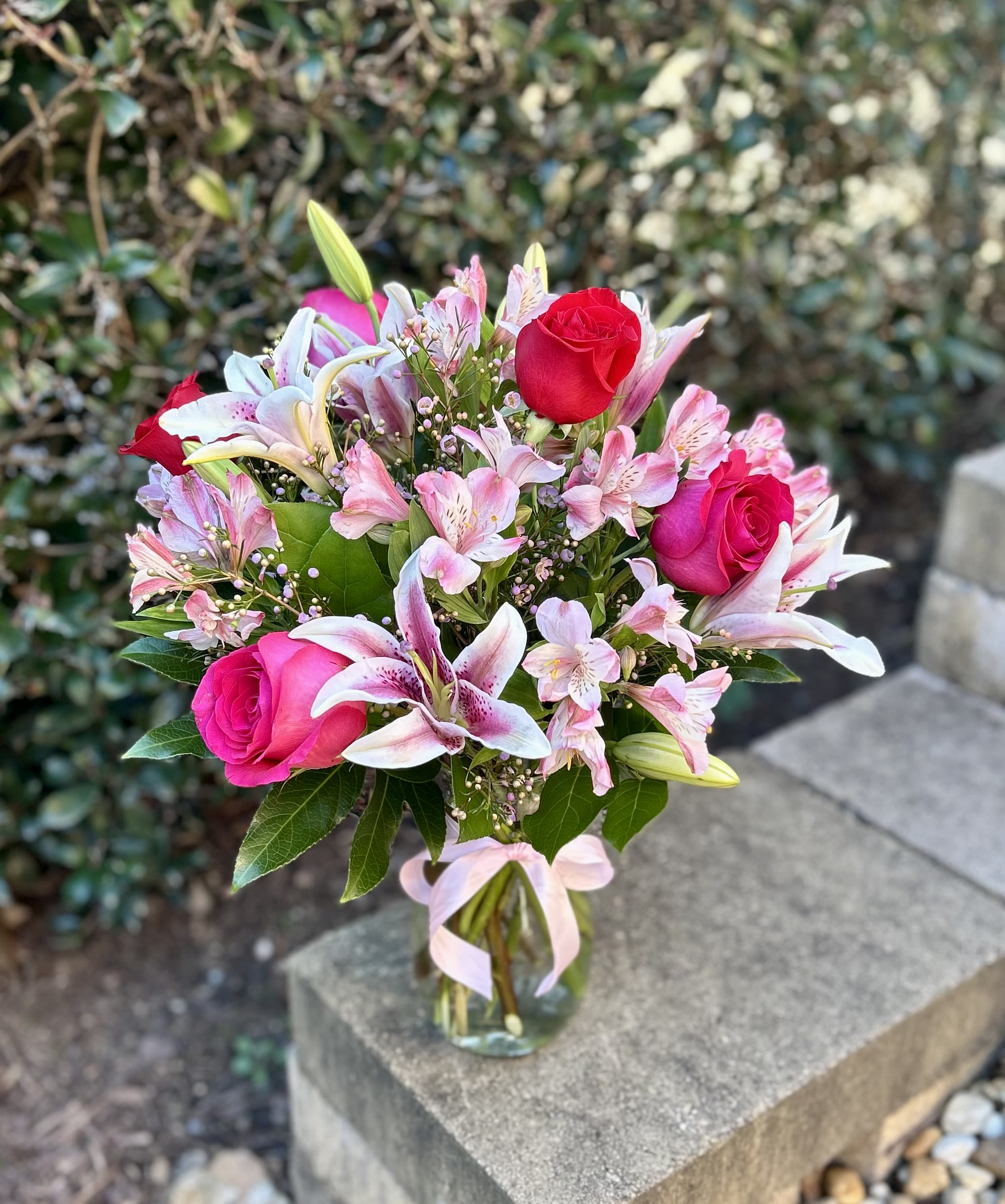 Bright Romance  - A graceful blend of pink and crimson roses nestled among soft lilies and delicate alstroemeria, Blushing Romance captures the feeling of a heartfelt moment—elegant, warm, and quietly enchanting. Perfect for celebrating love, appreciation, or a beautiful new beginning.