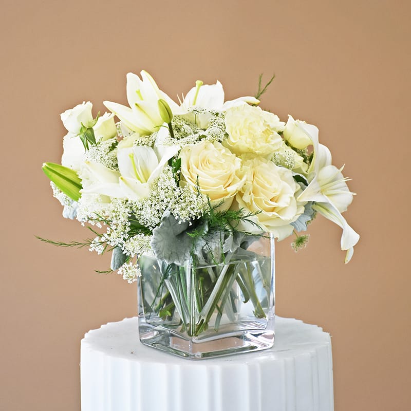 Snow White by Fillmore Florist | San Francisco Flower Delivery  - Experience the serene elegance of Snow White, a modern masterpiece designed for the discerning San Francisco eye. Fillmore Florist has crafted this arrangement to signify the highest levels of purity, grace, and sophisticated love. This "Quiet Luxury" design is curated for any high-stakes occasion, from corporate galas in SoMa to intimate Pacific Heights anniversaries.  Housed in a designer clear cubed glass vase, this monochromatic triumph features, white Lilies &amp; Roses, the classic foundation of luxury and romance. Delicate White Lisianthus, adding a ruffled, high-end couture texture. Silver Dusty Miller Greens, providing a soft, velvet-like bridge between the snowy blooms and the glass.  Fillmore Florist Strategic Difference     Verified Botanical Purity: We provide Exculpatory Proof of quality. White arrangements are the most difficult to deliver perfectly; our San Francisco flower delivery team audits every petal for "snow-white" integrity, ensuring no bruising or browning occurs during transit.     Architectural Cube Design: The cubed glass vessel provides a low-profile, "Gallery-Style" precision. This intentional shape is a hallmark of a professional San Francisco florist, designed to define a space rather than just decorate it.     Fresh Market Selection: We visit the local flower market daily to ensure your flower delivery in San Francisco utilizes only the most turgid, high-performance stems available in the Bay Area.  Approximate Dimensions: 9" H x 7" W