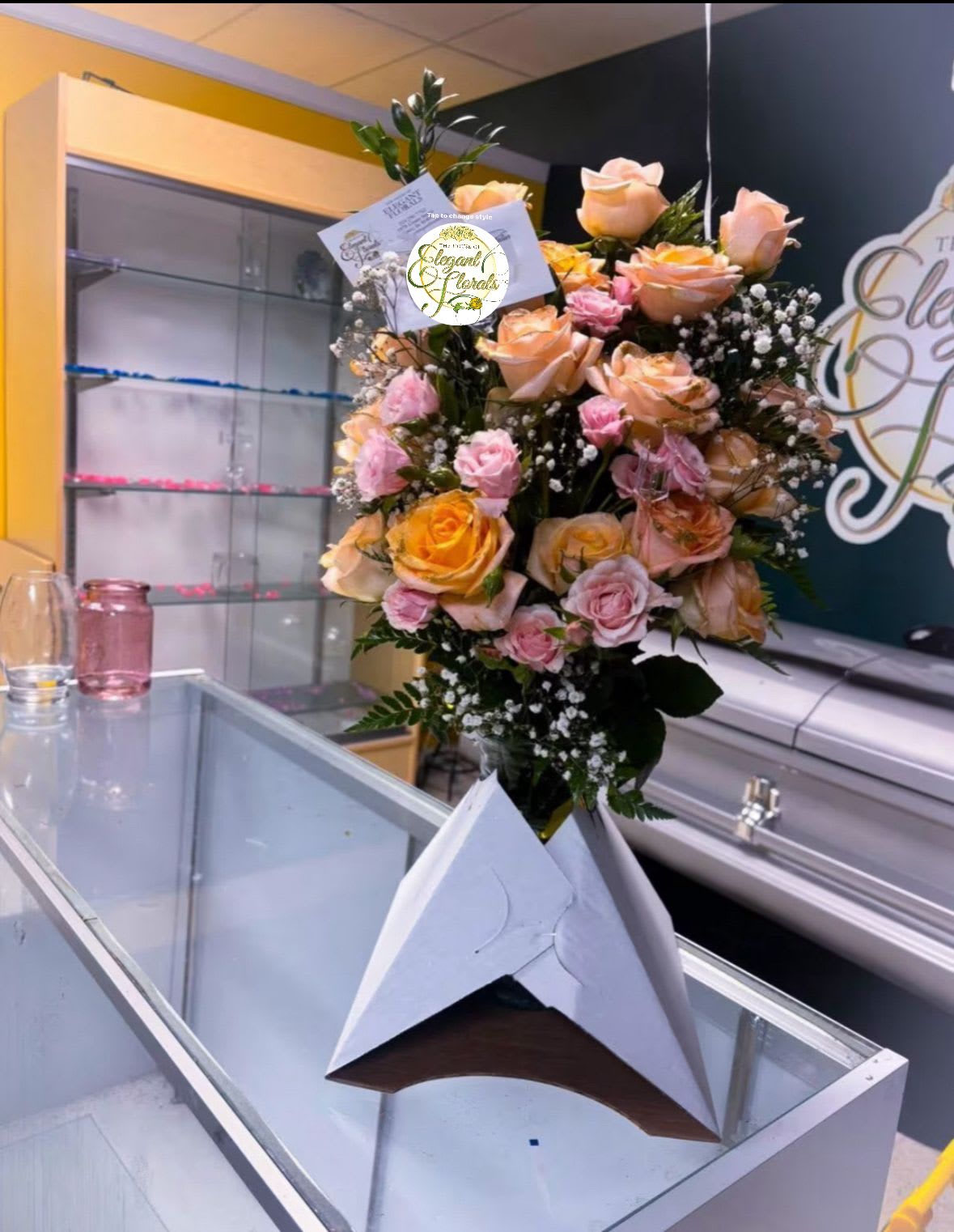 Peach &amp; Pink Rose Tower – Luxe Celebration Arrangement - Gracefully designed and elegantly structured, our Peach &amp; Pink Rose Tower is a standout floral arrangement ideal for both heartfelt sympathy gestures and joyful celebrations. This vertical masterpiece showcases a radiant medley of full-size peach roses, soft pink spray roses, lush greenery, and delicate baby’s breath, all arranged in a luxurious triangular base designed for stability and striking presentation.    Each bloom is carefully selected for freshness and visual harmony, creating a lush, full-bodied display that elevates any setting. Whether placed at a memorial service, gifted to a loved one, or used to honor a milestone moment, this arrangement speaks volumes with both elegance and warmth.    Details:    Includes: Peach roses, pink spray roses, baby’s breath, assorted greenery Dimensions: Approx. 24–30” tall Base: Designer triangular cardboard base with wooden accent, ideal for table or countertop display Custom message card included Perfect for: Sympathy, celebrations of life, anniversaries, grand openings, or elegant home décor