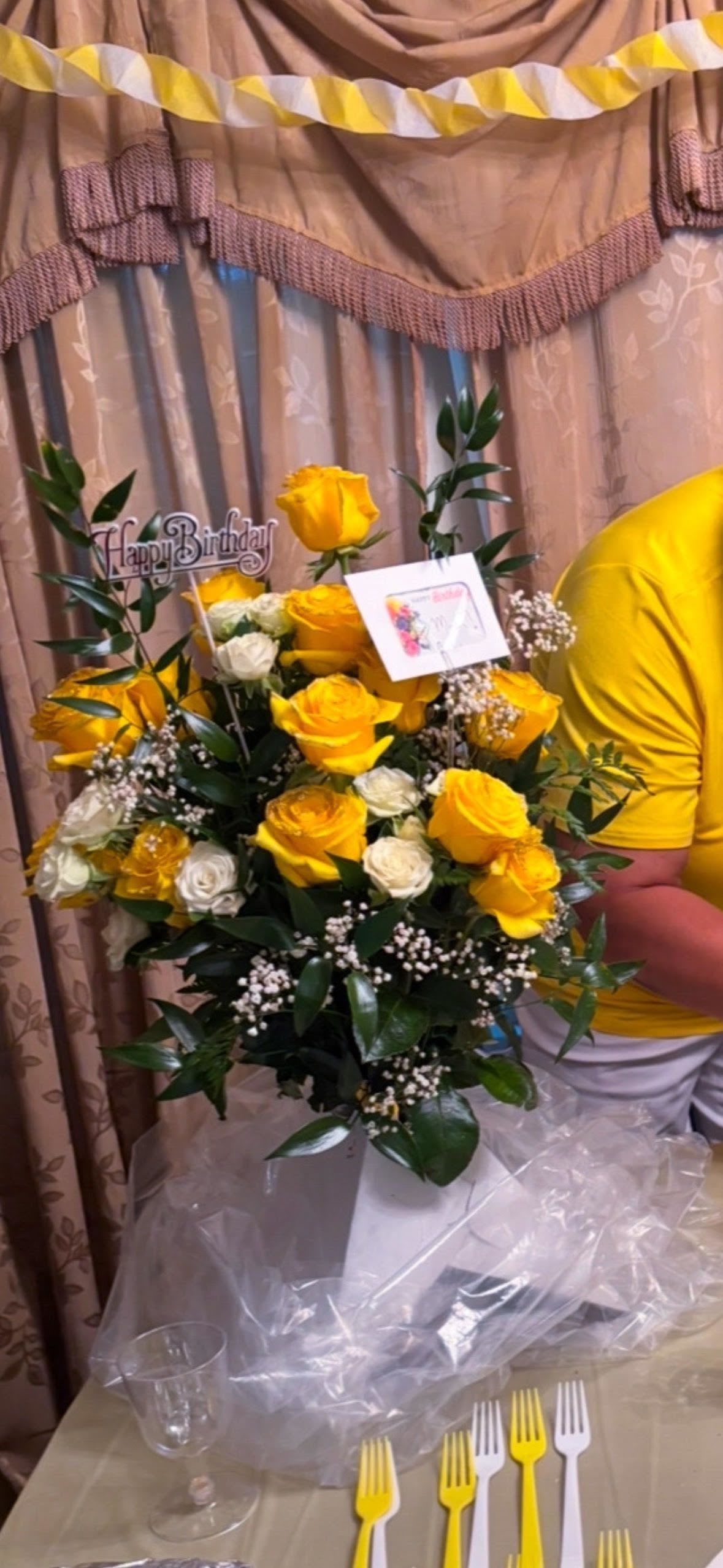 Sunshine Wishes – Yellow &amp; White Birthday Rose Arrangement - Brighten any celebration with our Sunshine Wishes rose arrangement – a joyful blend of golden yellow and creamy white roses, beautifully complemented by soft baby’s breath and lush greenery. Designed with height and elegance in mind, this cheerful bouquet makes a radiant statement at birthday parties, brunches, or any uplifting gathering.    Topped with a festive Happy Birthday pick and a custom message card, it arrives wrapped in clear cellophane for a polished presentation, making it the perfect surprise to light up someone’s special day.    Details:  Includes: Fresh yellow roses, white roses, baby’s breath, rich greenery  Accents: “Happy Birthday” pick and personalized card  Height: Approx. 26–30”  Base: Designer delivery stand with protective wrapping  Ideal for: Birthdays, celebrations, cheerful surprises  