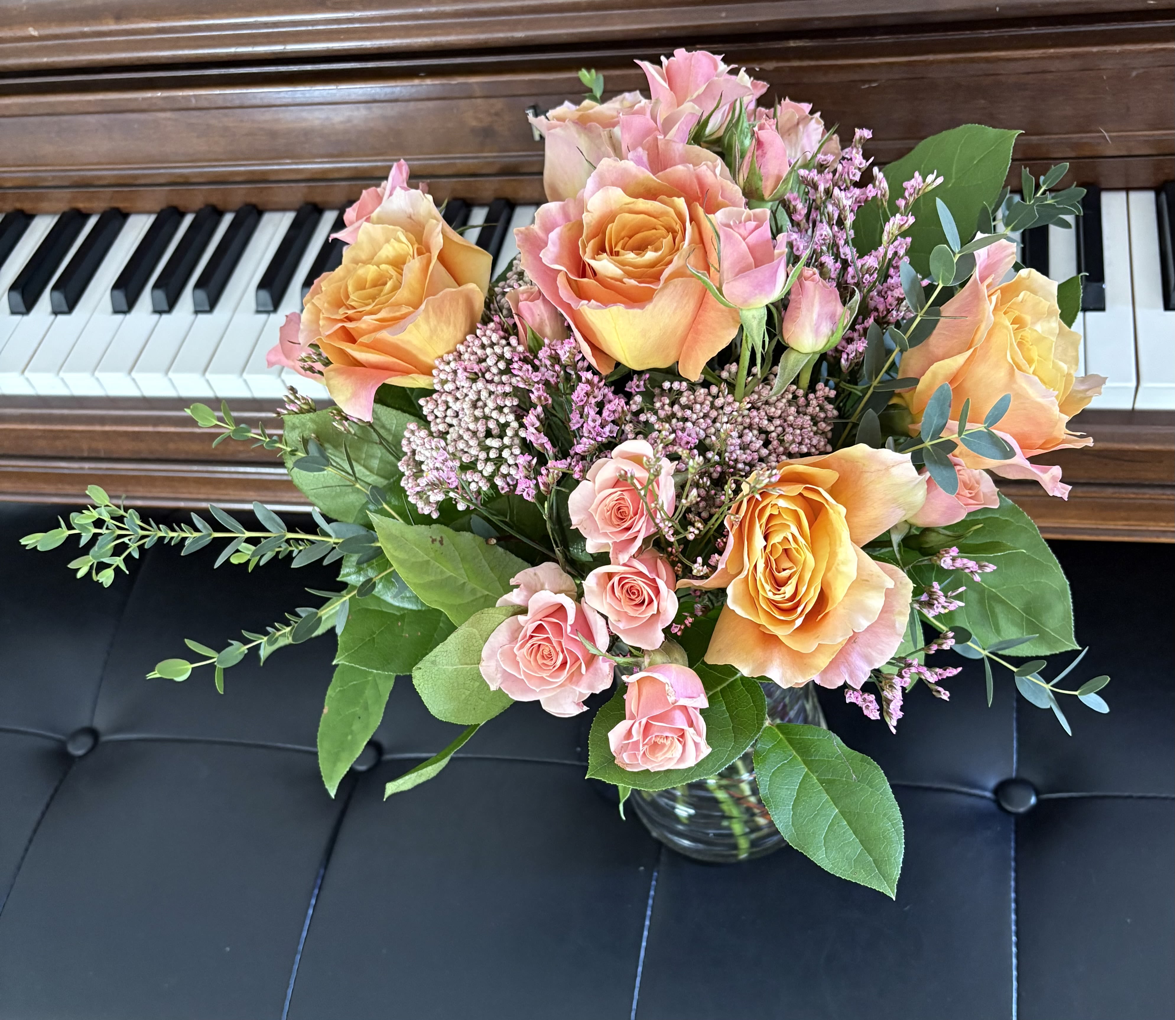 Rosy Reverie - A vibrant floral arrangement featuring large orange and pink roses with a gradient effect, complemented by smaller pink roses and clusters of tiny, delicate flowers in shades of pink and purple. The arrangement is accented with lush green foliage, creating a stunning and colorful display.