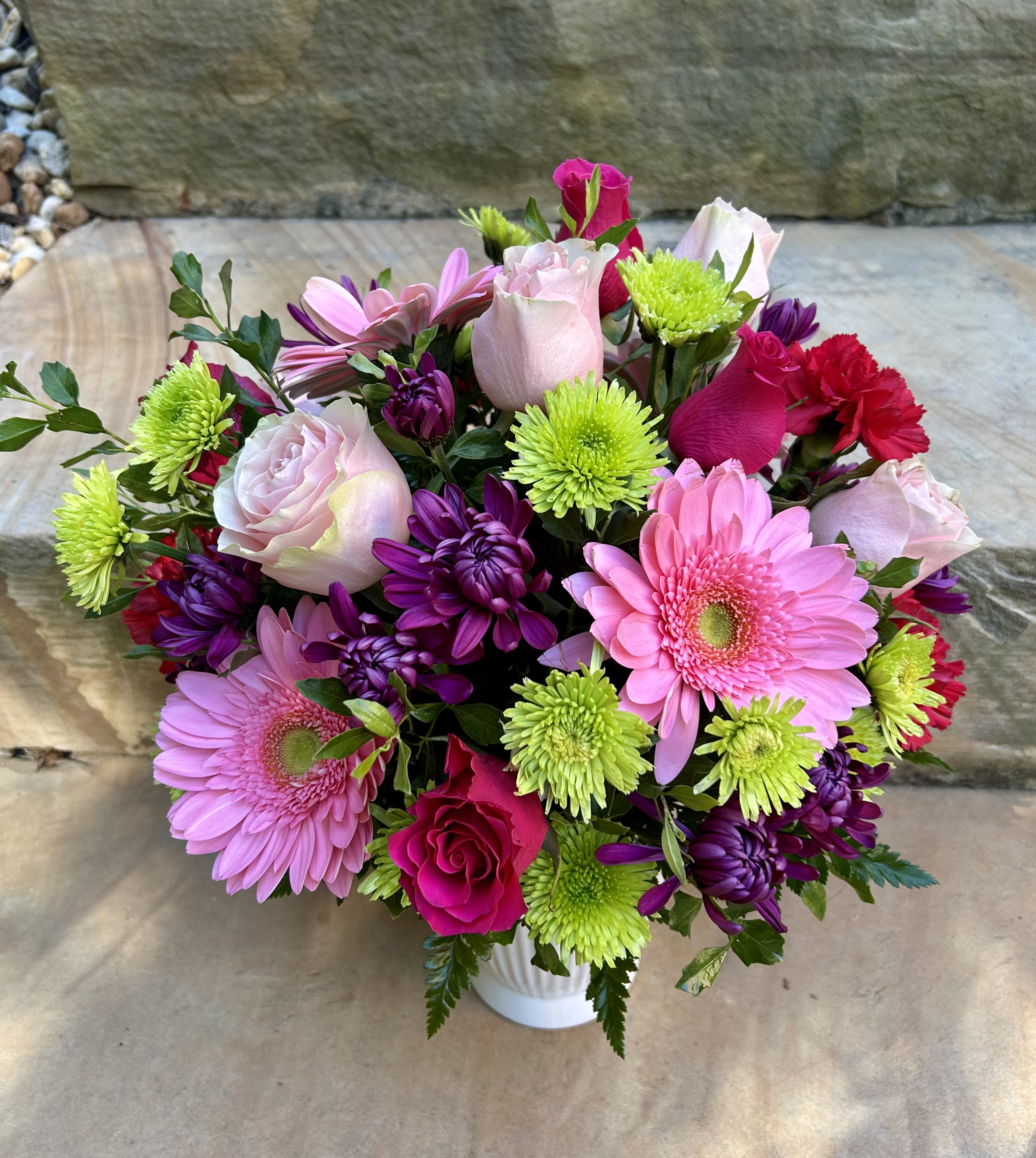Simply Sweet - A cute and bright arrangement of pink gerberas, pink and hot pink roses, hot pink spray roses, purple and green filler flowers arranged in a low profile white vase/pot. 