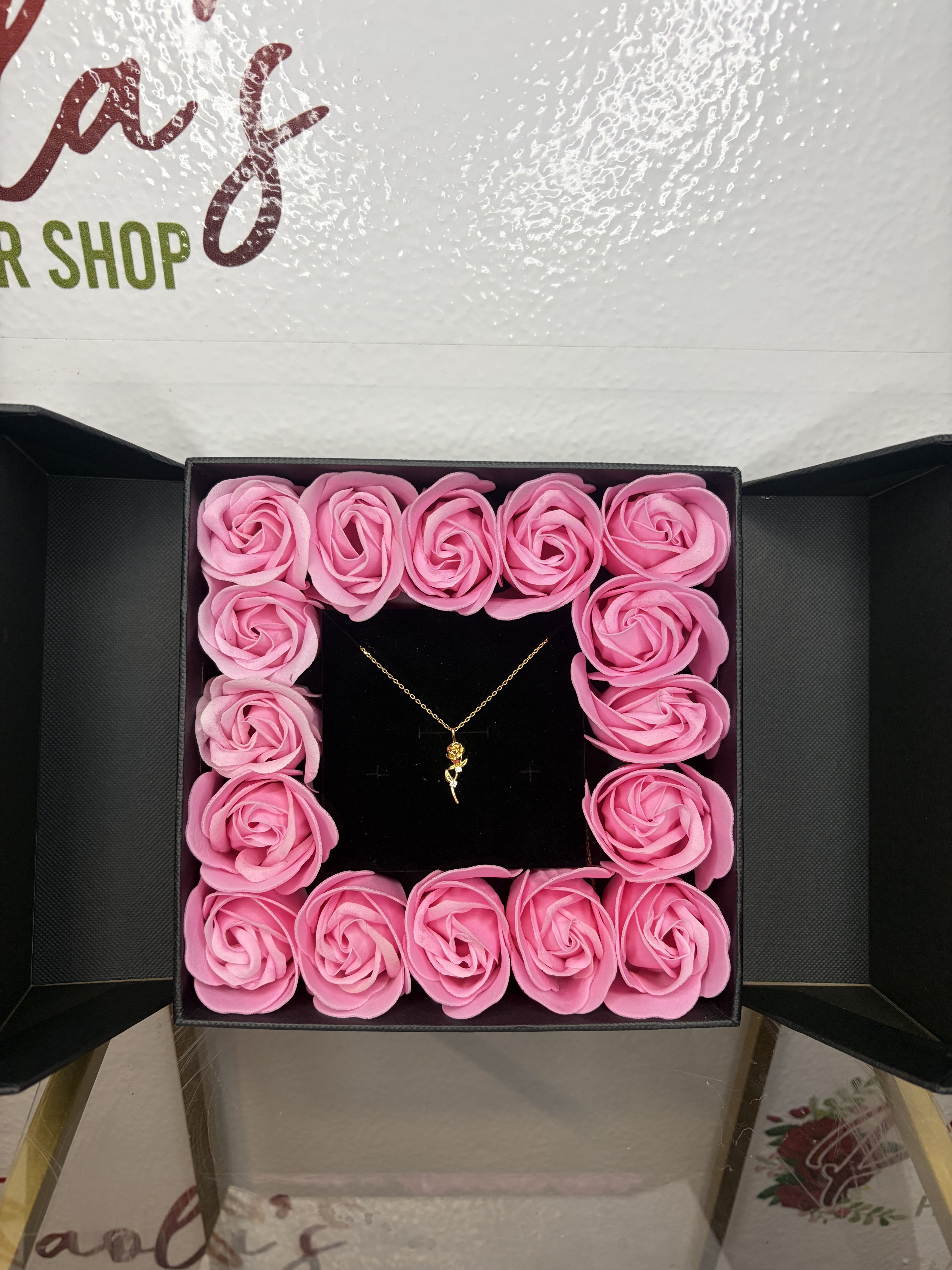 Rose Keepsake Box With Rose Pendant Necklace - A romantic gift that feels like opening a little treasure chest. This elegant black presentation box unfolds to reveal a frame of roses surrounding a delicate gold necklace at the center. The contrast of the deep velvet interior and pastel florals highlights the jewelry beautifully, making it perfect for anniversaries, birthdays, or a heartfelt surprise. Designed to impress the moment it opens — part keepsake, part jewelry display, all charm. *Not real roses in the gift box, available in pink or red*  Elegant and timeless, this Gold Dipped Rose Pendant Necklace captures the beauty of a blooming rose in full detail. Accented with delicate cubic zirconia stones along the stem, it adds a subtle sparkle to any outfit. A perfect gift to symbolize love, grace, and everlasting beauty.  Material: Gold dipped, cubic zirconia Color: Gold Length: 16"  Closure: Lobster clasp Style: Romantic, elegant, feminine Ideal for: Everyday wear, special occasions, or gifting