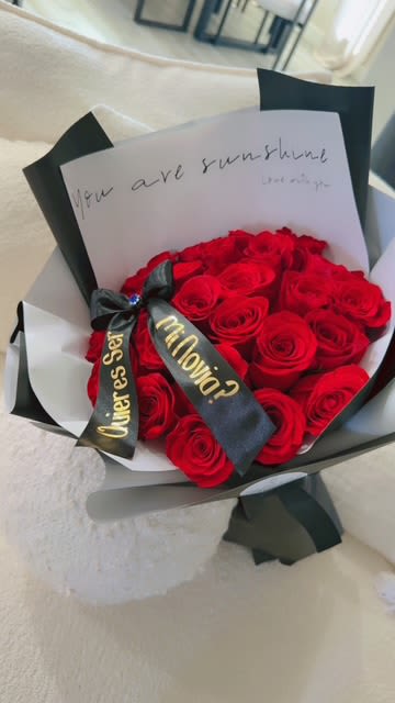 Be Mine Proposal Bouquet - 24 red Roses!  When words aren’t enough—let the roses do the asking. The Be Mine Proposal Bouquet is a bold and unforgettable way to ask that special someone to be yours. Featuring a luxurious arrangement of deep red roses, wrapped in modern black and white tones, and a personalized ribbon with the golden question: "¿Quieres ser mi novia?" (Will you be my girlfriend?).   Includes a message card that reads "You are my sunshine."  Elegant black satin ribbon with gold lettering.  Delivery available with discreet or scheduled timing for the perfect surprise.   Make your moment unforgettable. Ask with roses.