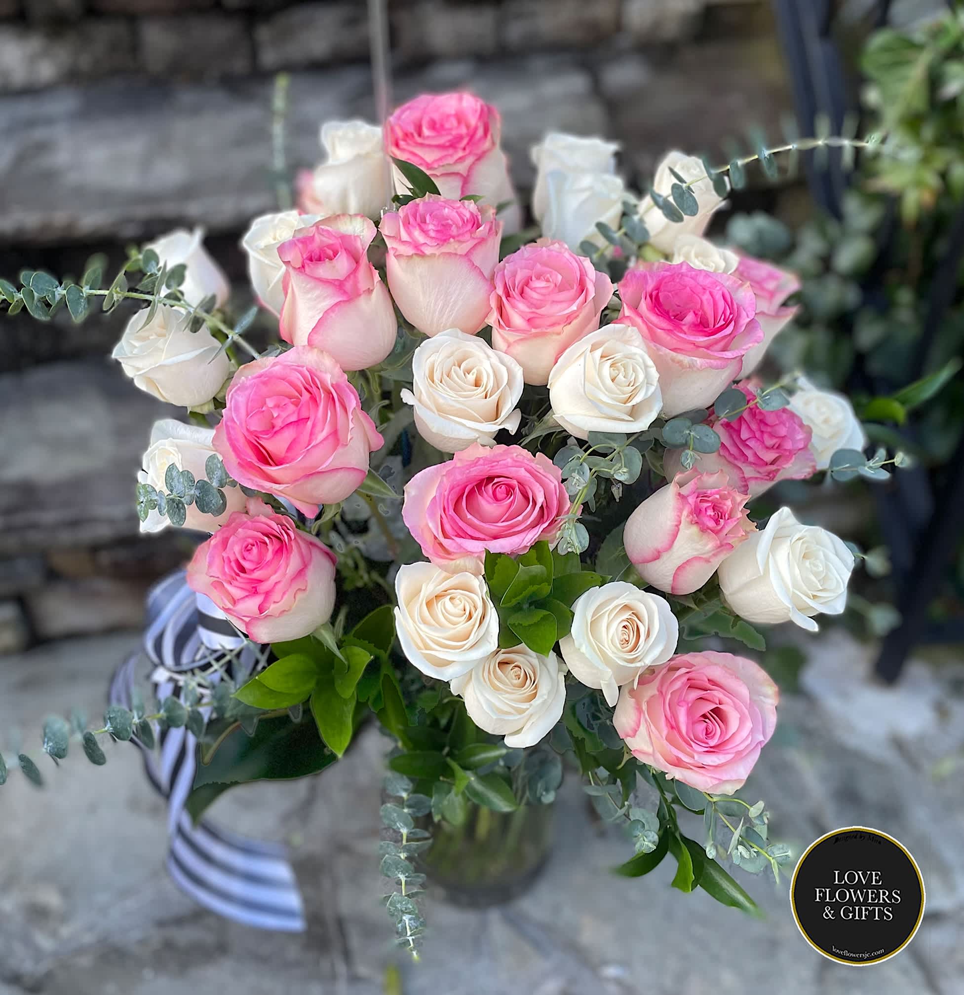 Arrangement of pink and white roses in a clear glass vase with striped ribbon