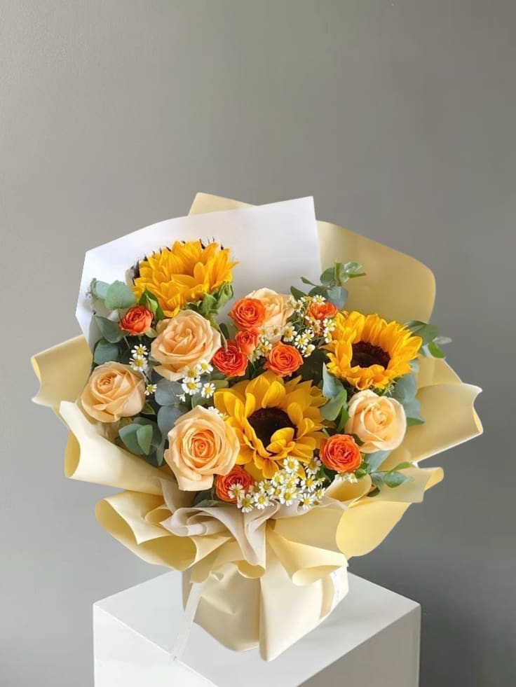 Heart Of Gold  - This radiant bouquet combines cheerful sunflowers with soft peach roses to create a warm and uplifting floral design. The bold, golden petals of the sunflowers bring a sense of happiness and positivity, while the peach roses add a gentle touch of elegance and romance. Together, these blooms create a beautifully balanced bouquet that feels both bright and refined.
