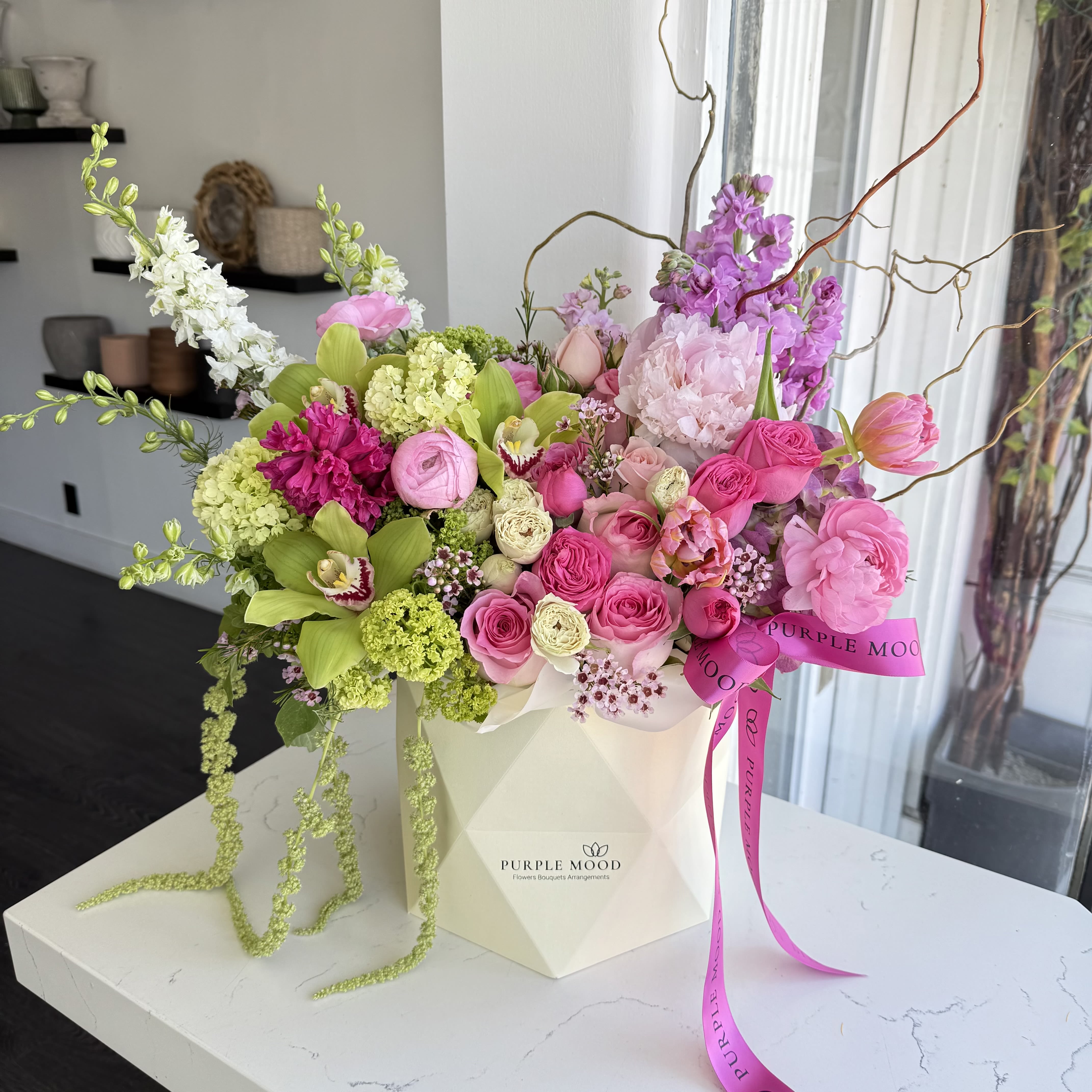 Green Splash - Geometric box with roses, and others flowers. Container size D7.75’x H8.25′ All around arrangement with no lid in back. Box included wet floral foam inside, box doesn’t require vase.