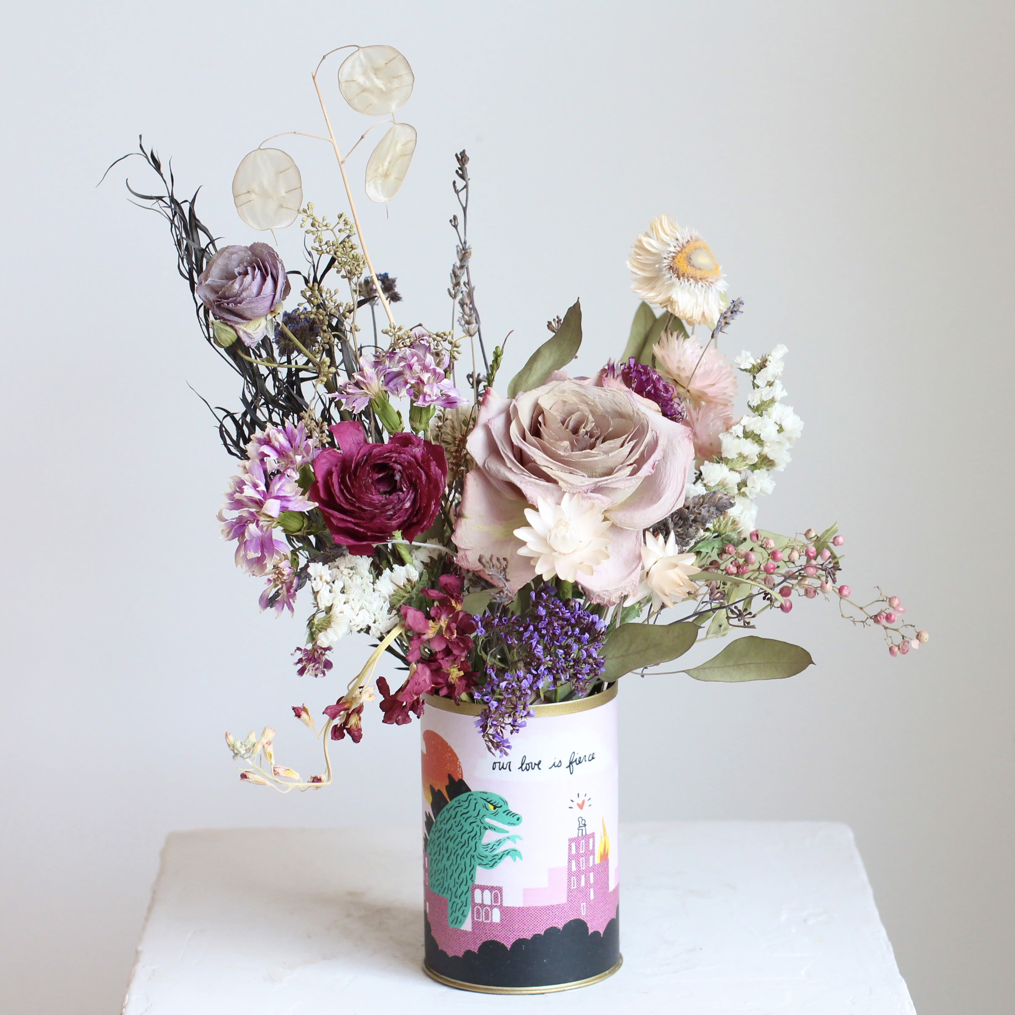 "Our Love is Fierce" Dried Floral Arrangement - A charming blend of rustic elegance and sentimental charm, this dried floral arrangement is beautifully displayed in an Our Love is Fierce tin. Featuring a thoughtfully curated mix of preserved blooms, delicate grasses, and textured foliage in warm, bright tones, this arrangement exudes timeless beauty. Perfect for gifting or adding a touch of vintage-inspired romance to any space, it’s a lasting expression of love and appreciation