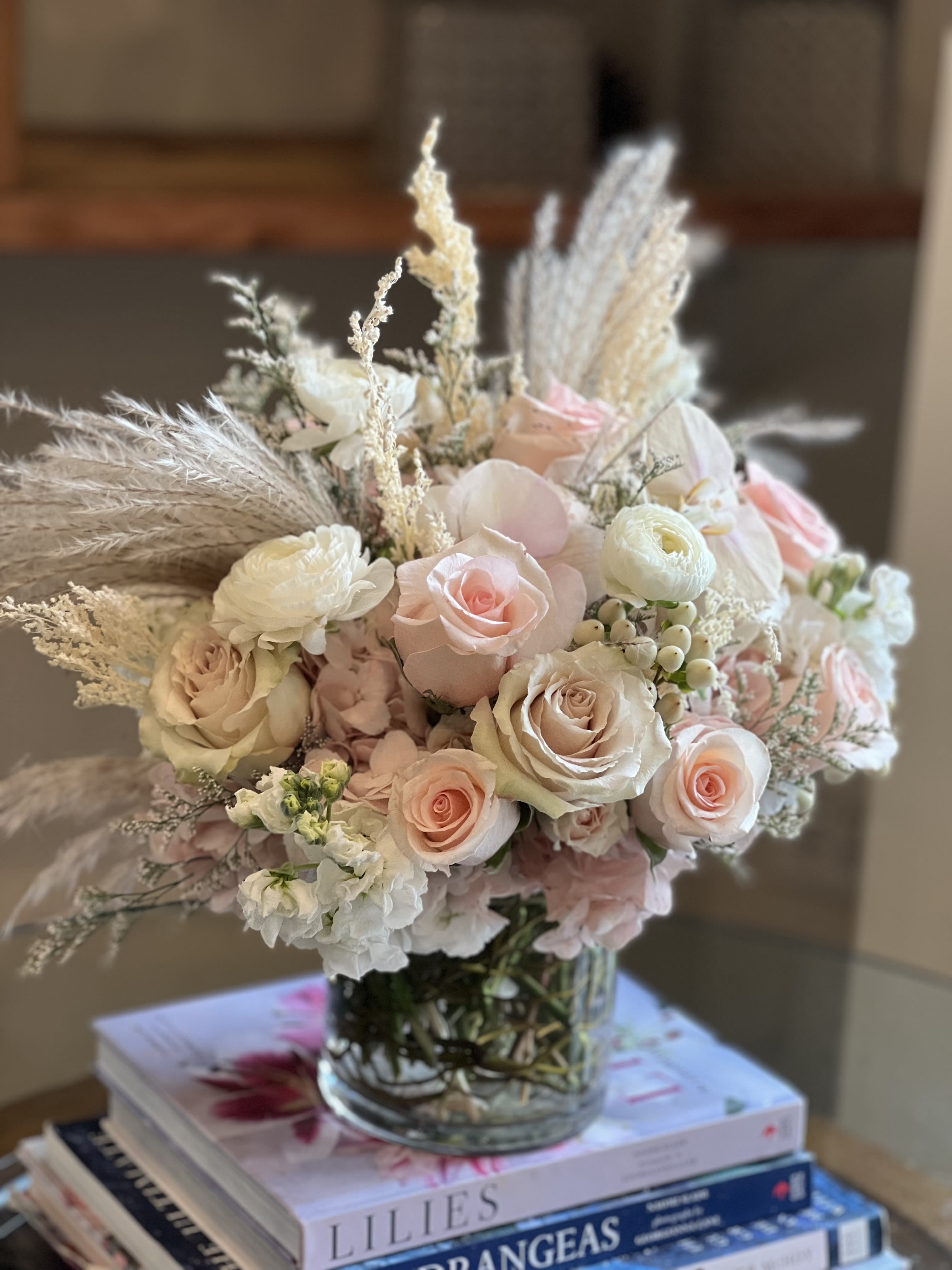 Angelic Pink  - Flowers: light pink roses, quicksand roses, light pink hydrangea, white ranunculus, pampas grass, dried rice flower, white stock, misty white, and peach orchids. Arranged in a 5x5 glass cylinder vase accented with curly willow.
