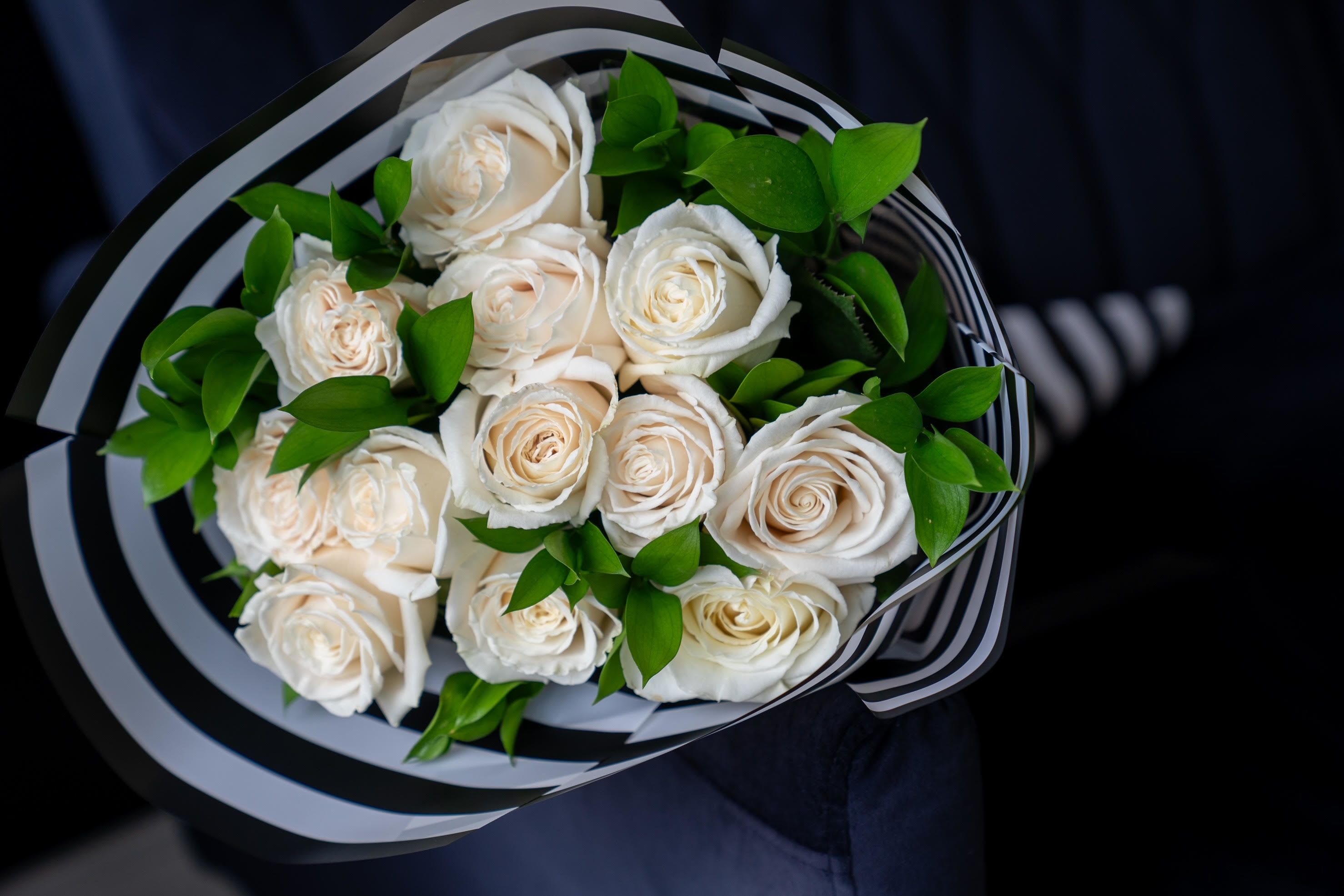 Dozen Long Stemmed White Rose Bouquet -  White Rose Bouquet is a timeless symbol of purity, elegance, and grace. This exquisite arrangement features long-stemmed white roses, each carefully selected for its pristine beauty and delicate petals. The classic white roses are thoughtfully arranged to create a serene and sophisticated display, perfect for expressing love, admiration, or respect. Whether for a wedding, anniversary, or simply to brighten someone’s day, this bouquet embodies the perfect balance of beauty and simplicity.   Arrangement Includes: -Fresh Cut Long Stemmed White Roses (12 count, 60"-70") -Assorted Greenery -Custom Paper Wrapping -Custom Greeting Card -Care Instructions