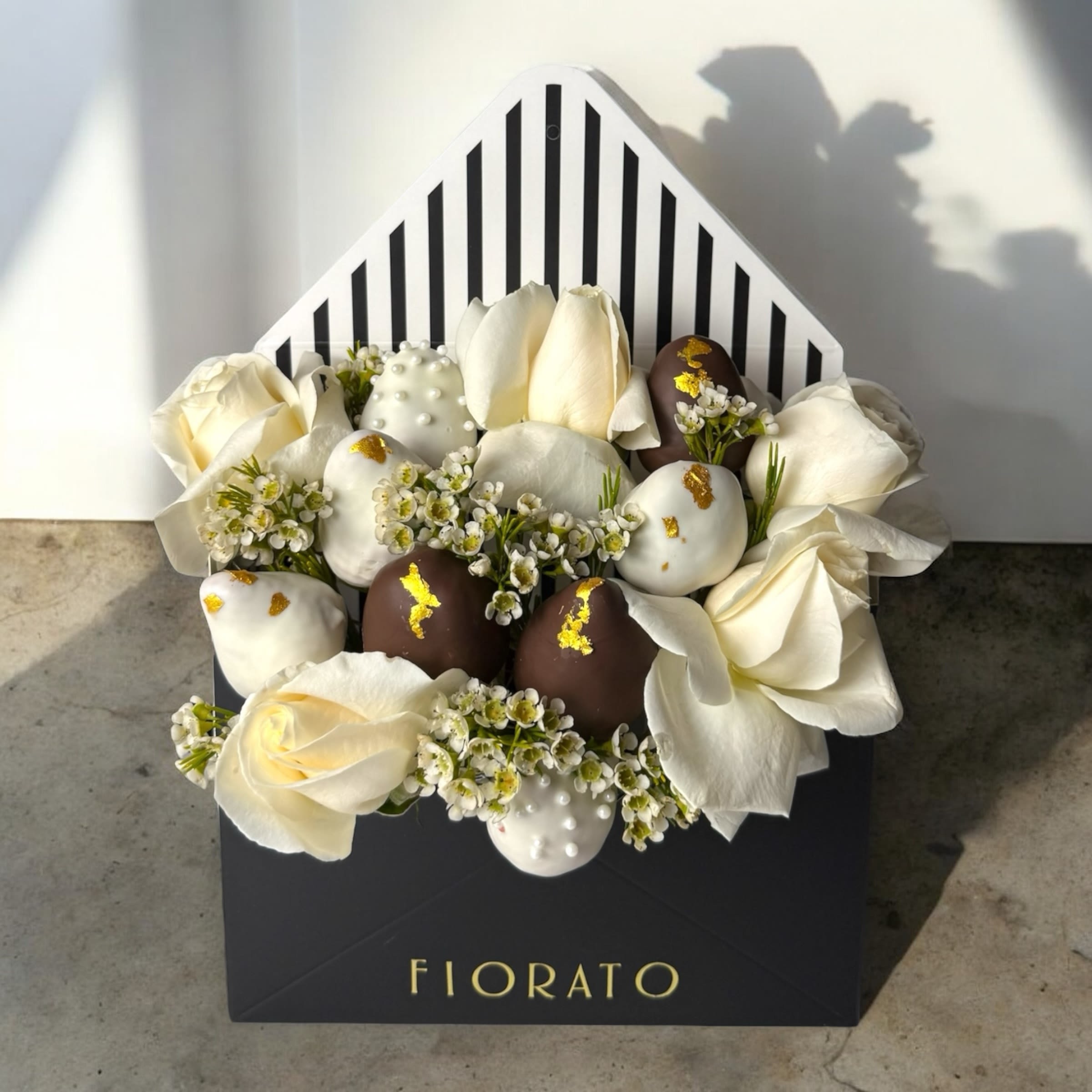 Ivory Melody - Ivory Melody es una sinfonía de elegancia y dulzura. Un delicado arreglo floral en tonos marfil y blanco, con rosas frescas, flores silvestres y fresas bañadas en chocolate blanco y negro, acentuadas con oro comestible. Perfecto para celebraciones sofisticadas, regalos de agradecimiento reflexivos o simplemente para alegrar el día a Mamá.