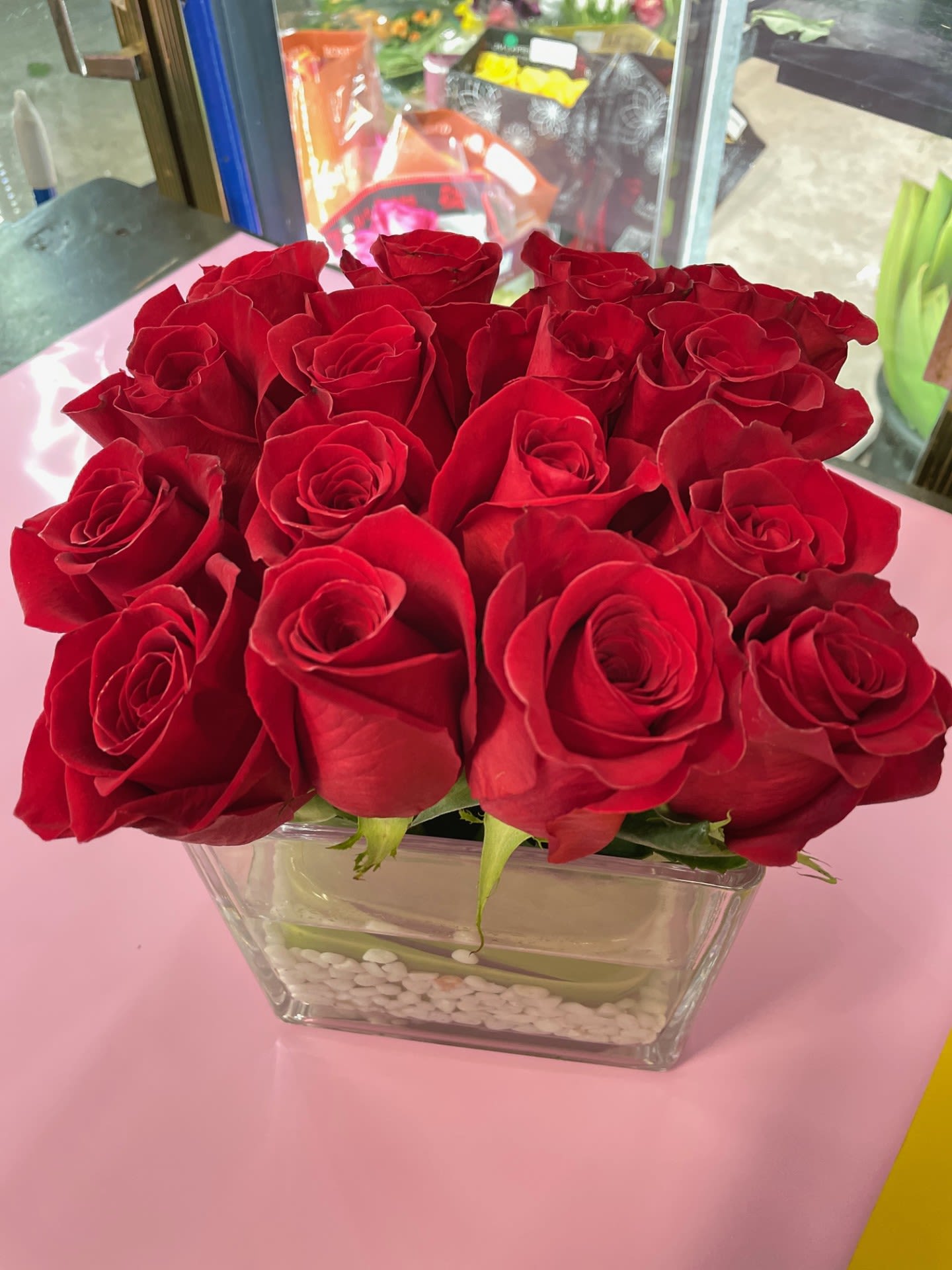 16 in Red - 16 Perfectly arranged Red Roses in a 6X6 Glass vase, lined and designed with White Pebbles at the base.
