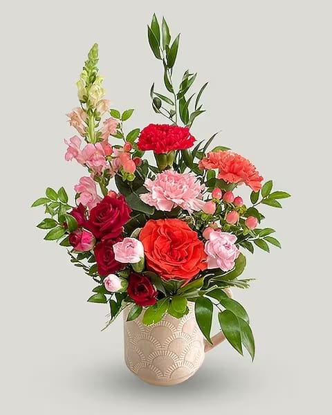A Cup of Love - A cozy arrangement filled with long lasting carnations, a snapdragon, hypericum berries, and roses. This Cup of Love is styled in a keepsake mug (may differ from photo), and will put a smile on your loved ones face!