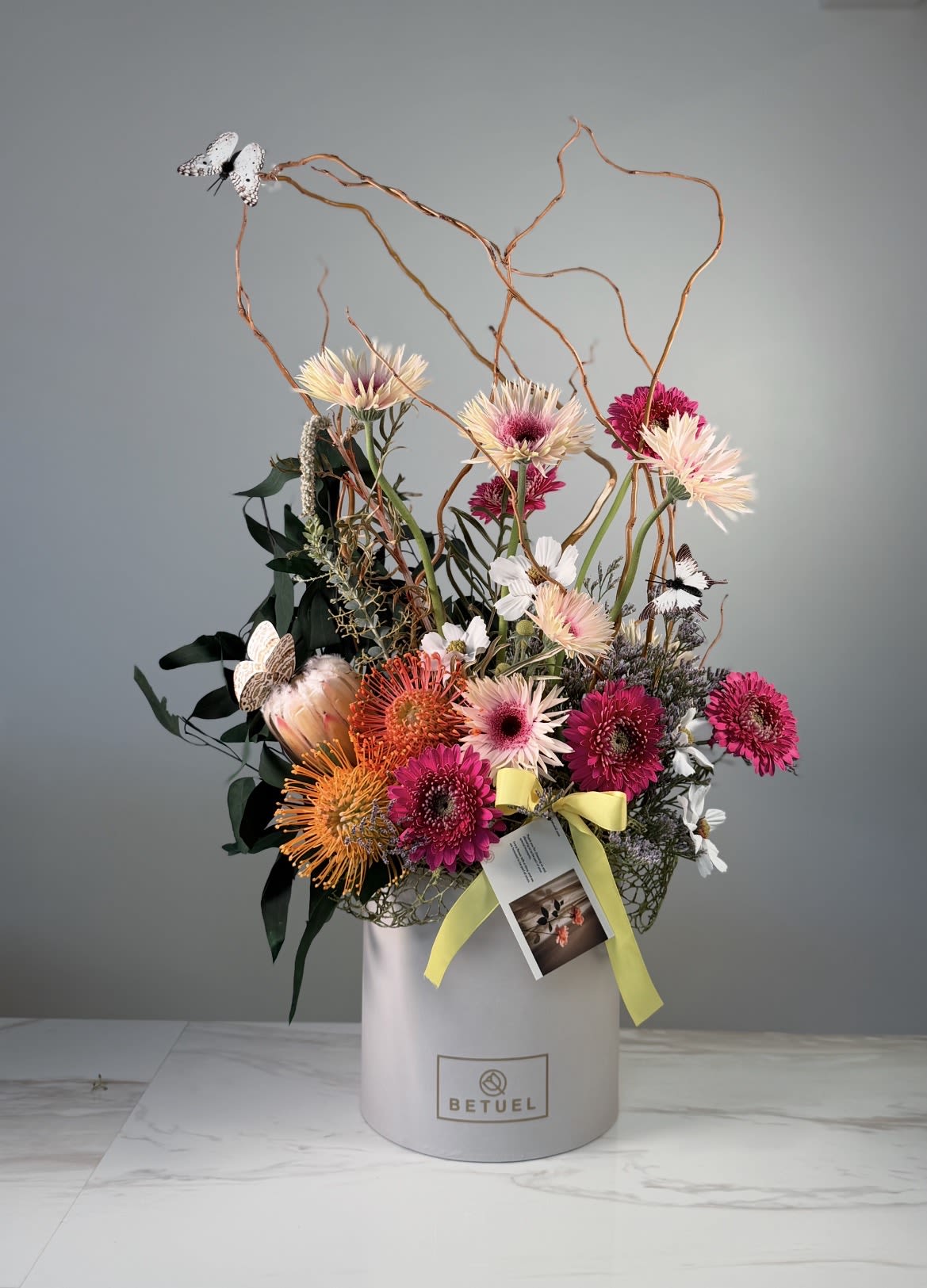 Betuel essence - This floral arrangement by Betuel stands out for its vibrant mix of textures and colors, integrating exotic elements with classic flowers to create a “wid” and artistic design 