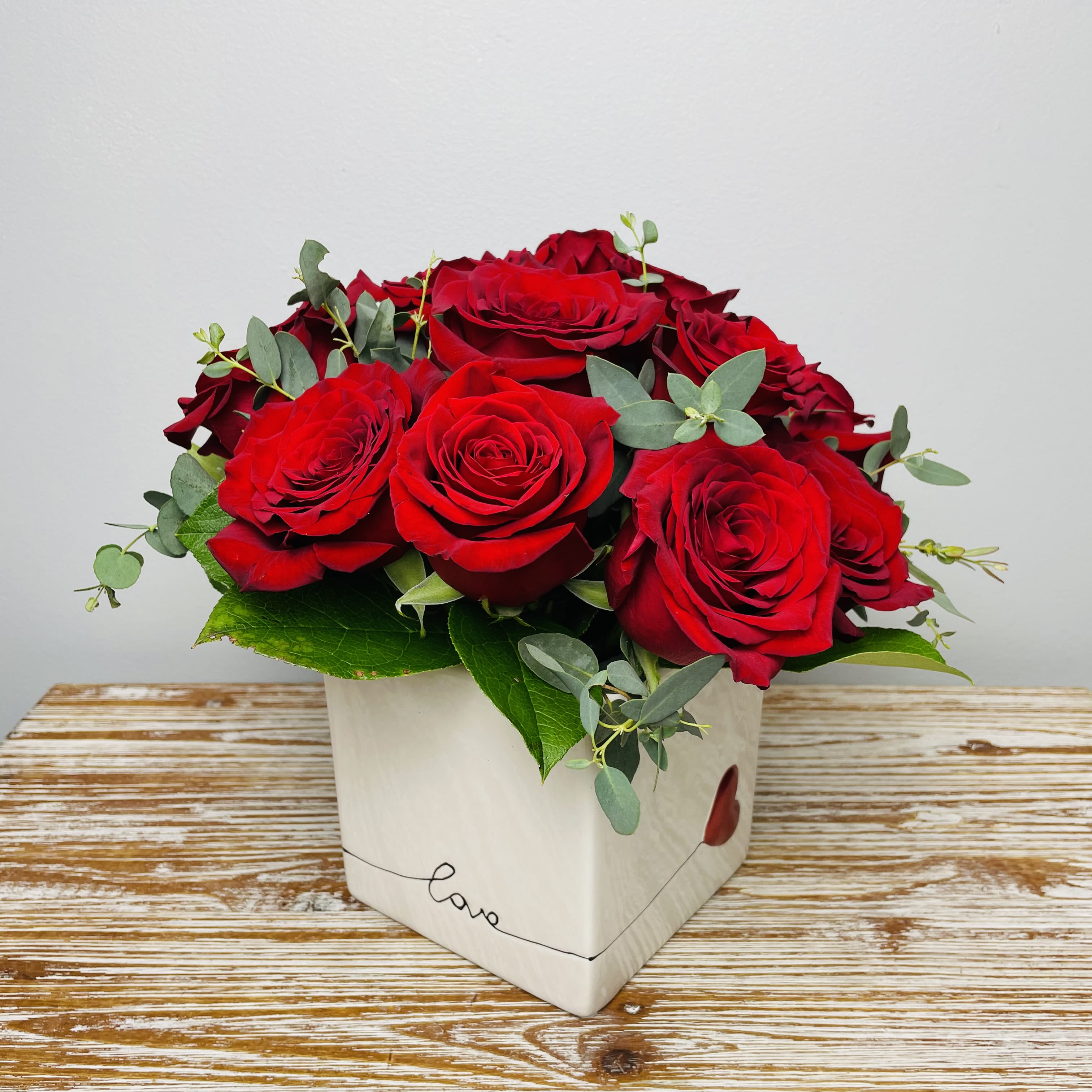 Modern Love - The modern twist on a dozen red roses! Twelve beautiful red roses accented with premium greens in a white ceramic love cube.   Approximately 10" Tall  Container Country of Origin: China Flower Country of Origin: Ecuador and/or Columbia