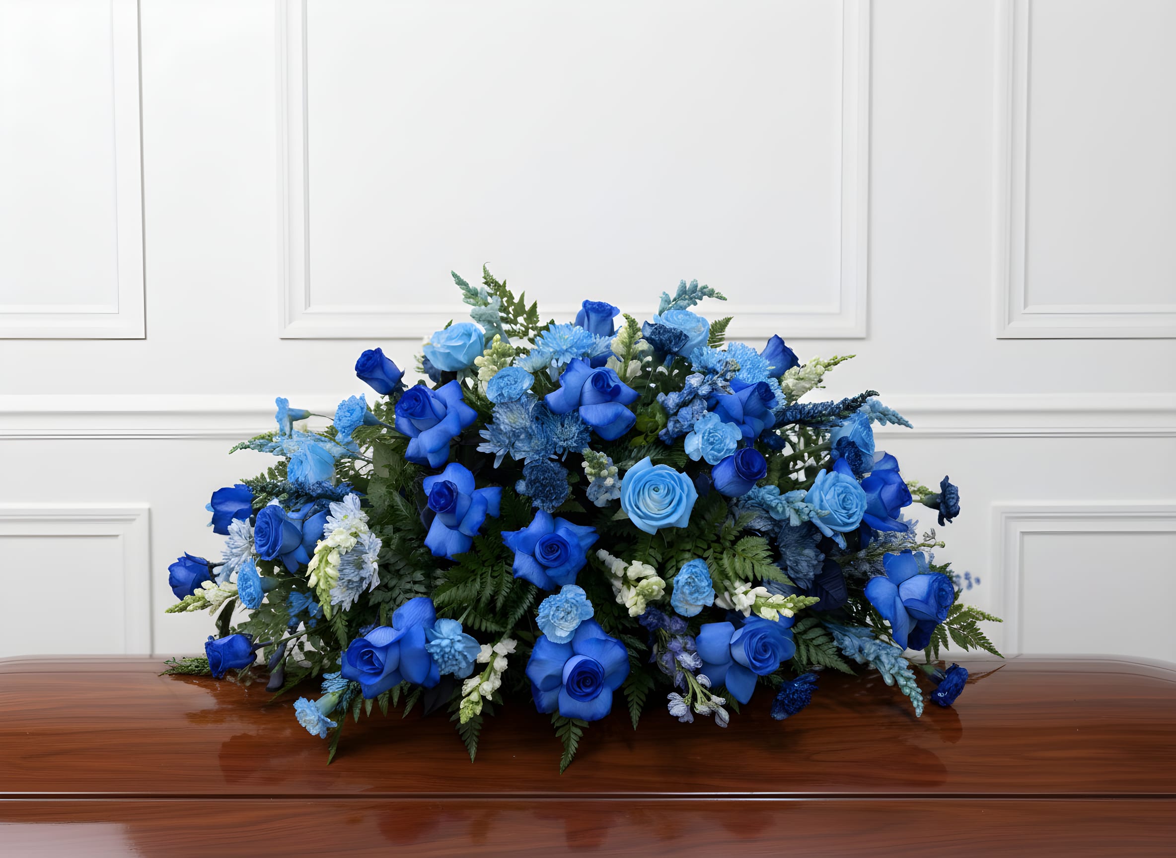 Peaceful Skies Casket Spray - A graceful casket spray arranged in soothing shades of blue, complemented by soft accent blooms and fresh greenery. This serene tribute symbolizes peace, comfort, and everlasting remembrance, offering a calm and heartfelt farewell to a cherished life.