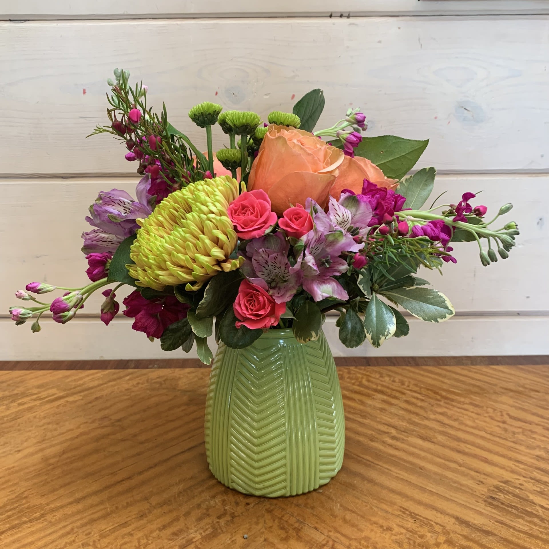 Celebrating Mom - A bright mother's day arrangement with apricot roses, magenta stock, green cremon chrysanthemum, hot pink spray roses and lavender alstroemeria arranged in a lime inverted triangle glass vase with seasonal filler flower. Approximately 11" wide and 12" tall.
